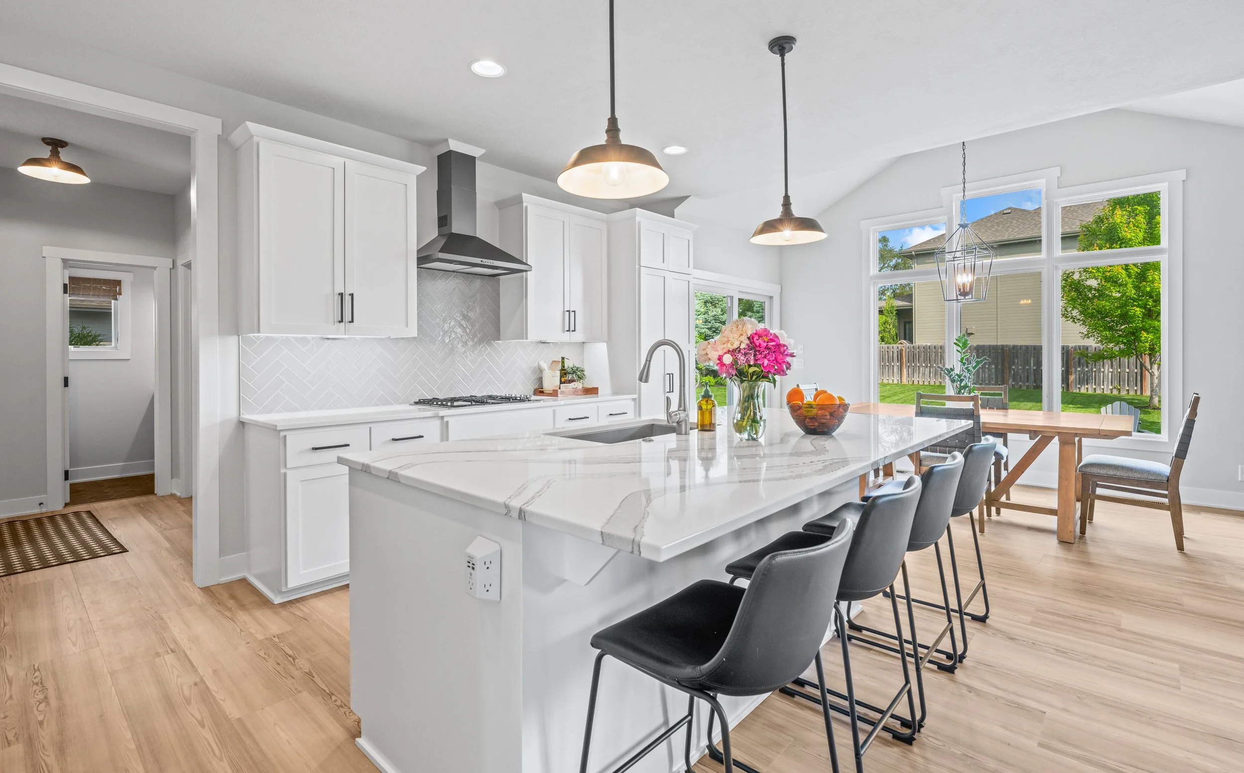 Professionally edited real estate photo of a bright white kitchen with quartz island, pendant lighting, and open dining area
