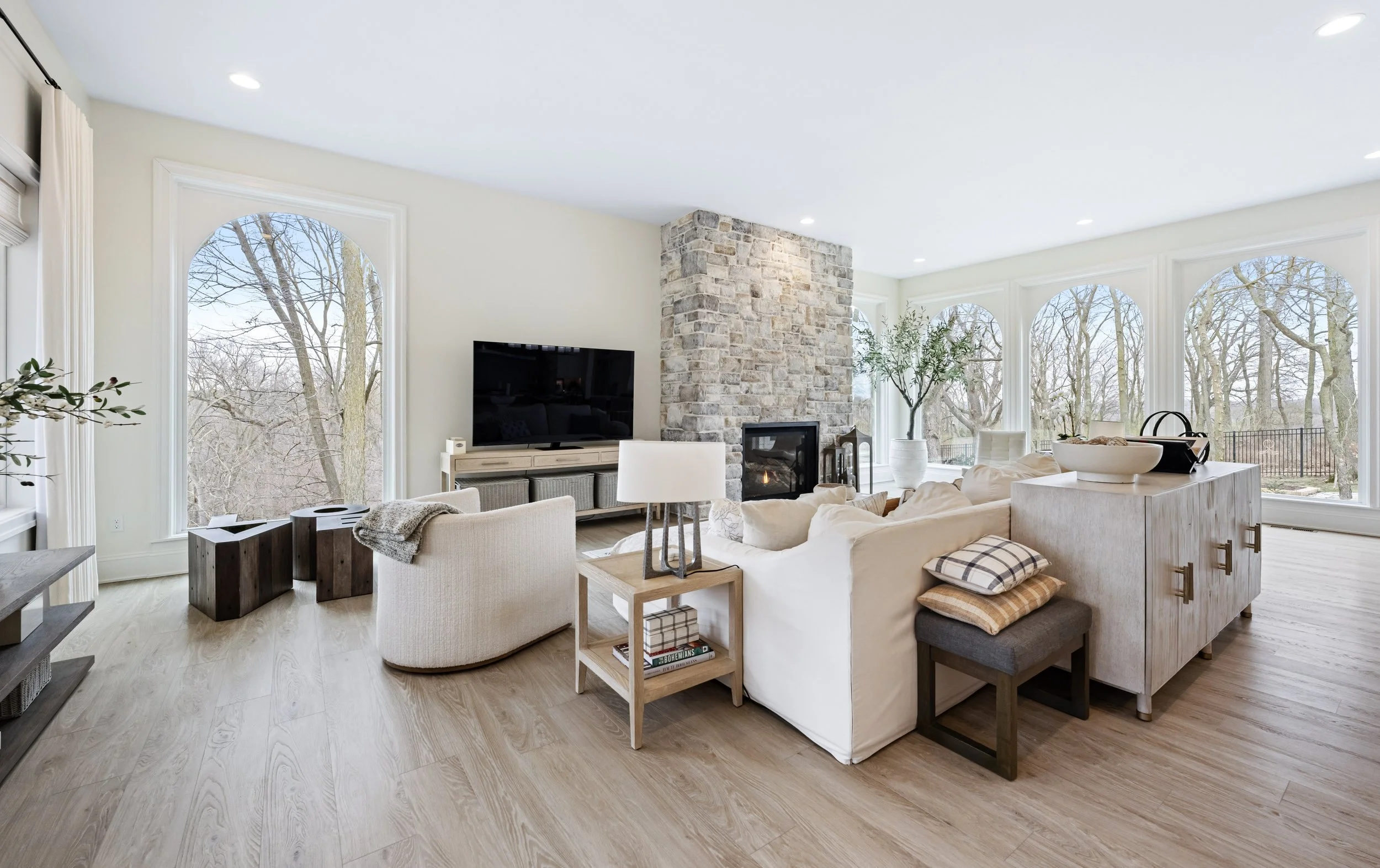 Bright living room with tall arched windows, a stone fireplace, and light wood floors, shot by a professional real estate photographer with balanced window light