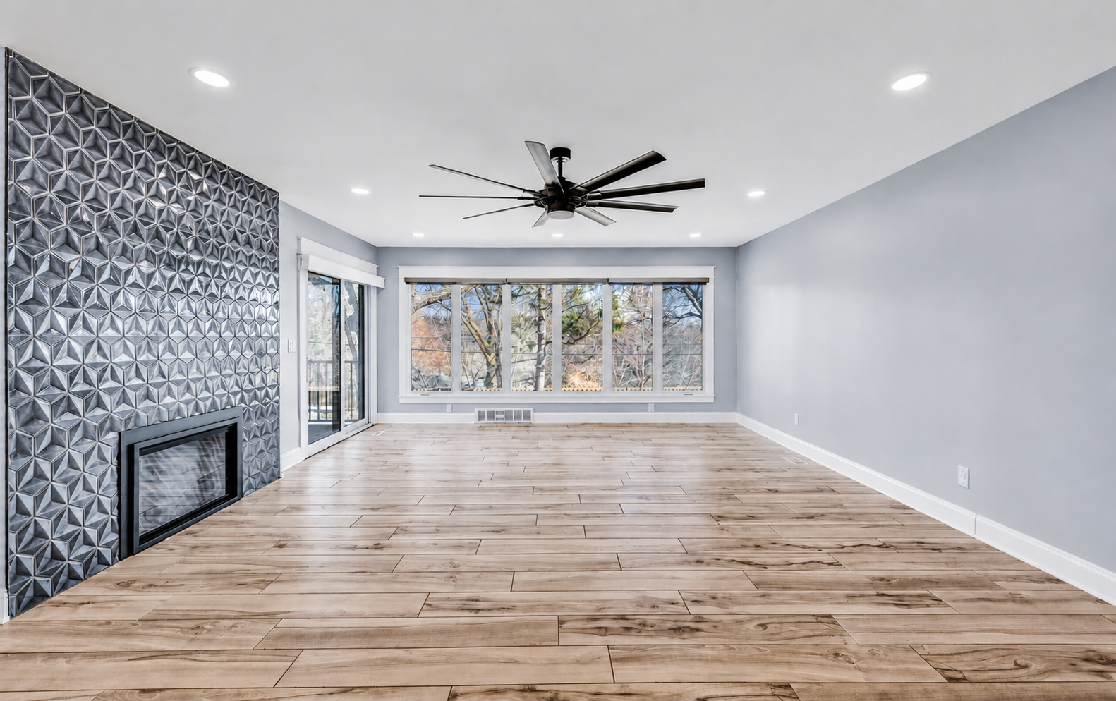 Vacant living room featuring geometric 3D tile fireplace wall, large picture windows, and luxury vinyl plank flooring — HDR real estate photography by Gabriel Khan Media