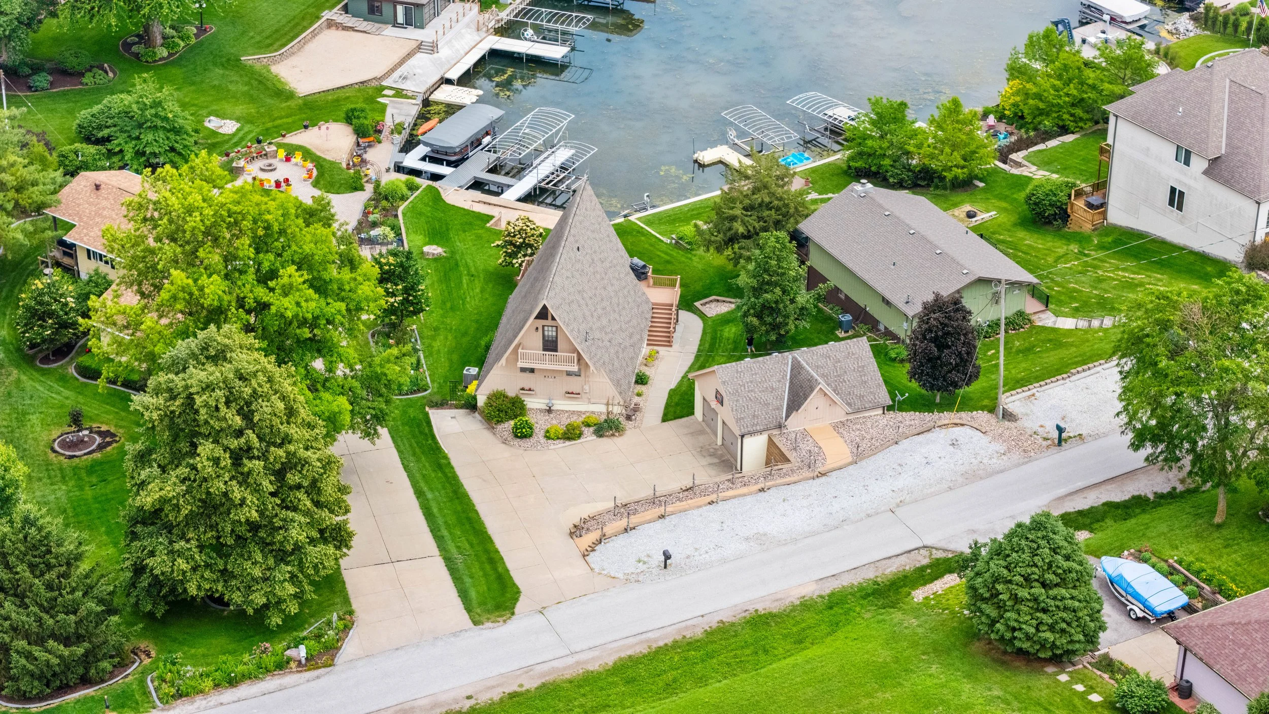 Aerial drone photo showing a waterfront property with a distinctive roofline, lot boundaries, and adjacent lake access.