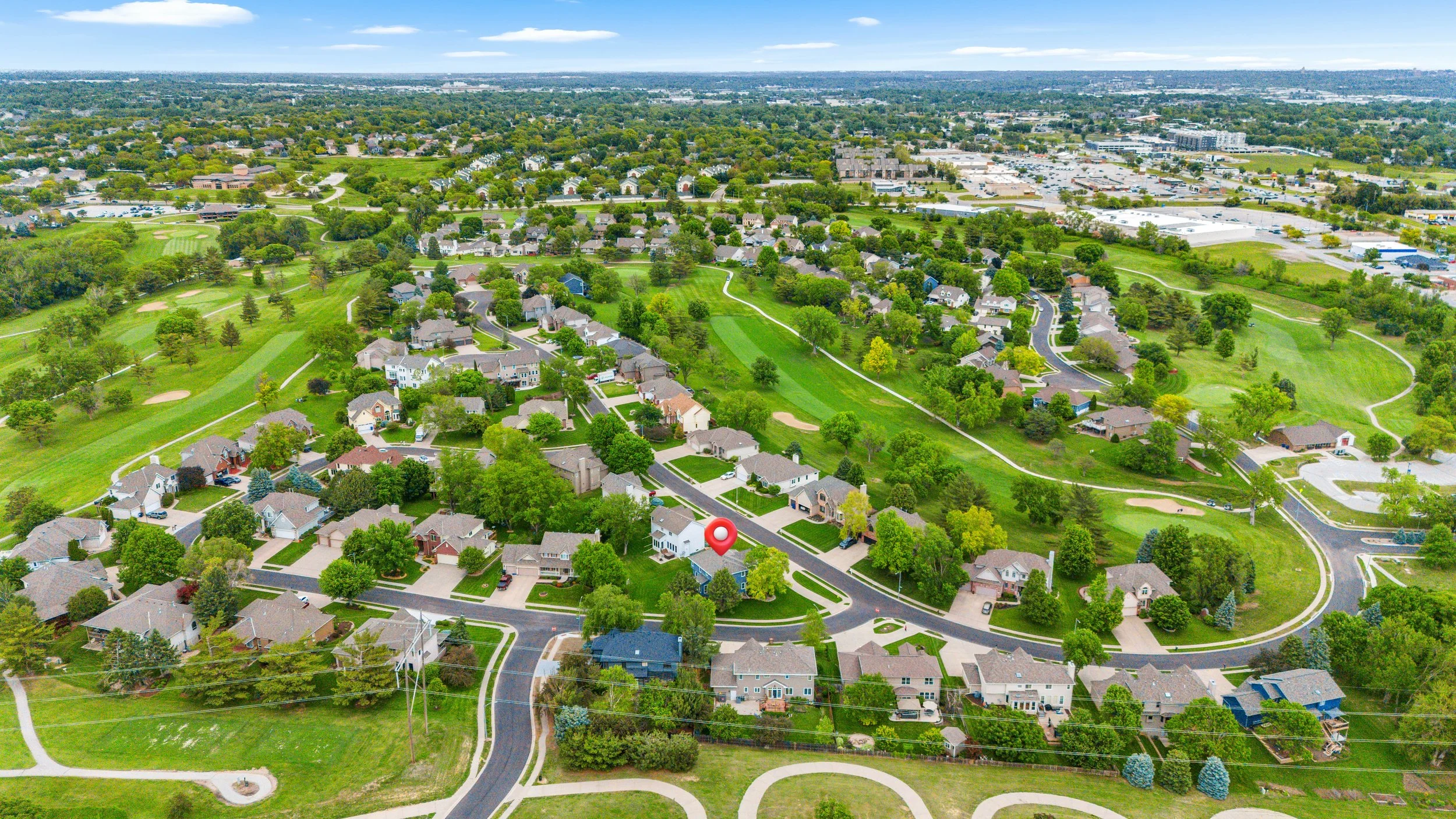 Wide aerial drone photo showing a residential property in context of surrounding neighborhood, streets, and open green space.