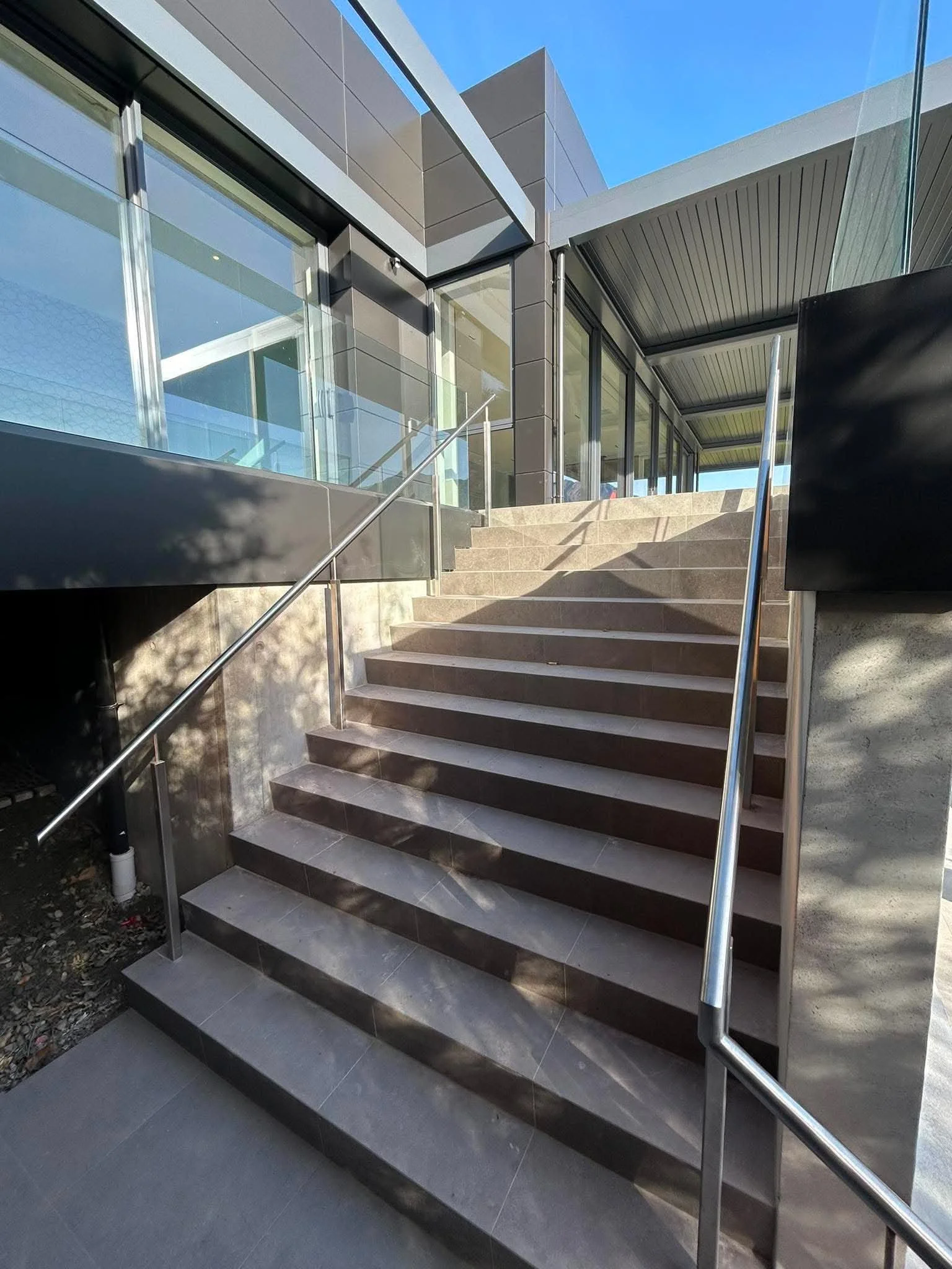 Exterior view of a modern building with stairs, glass windows, and metal railings, under a bright blue sky.