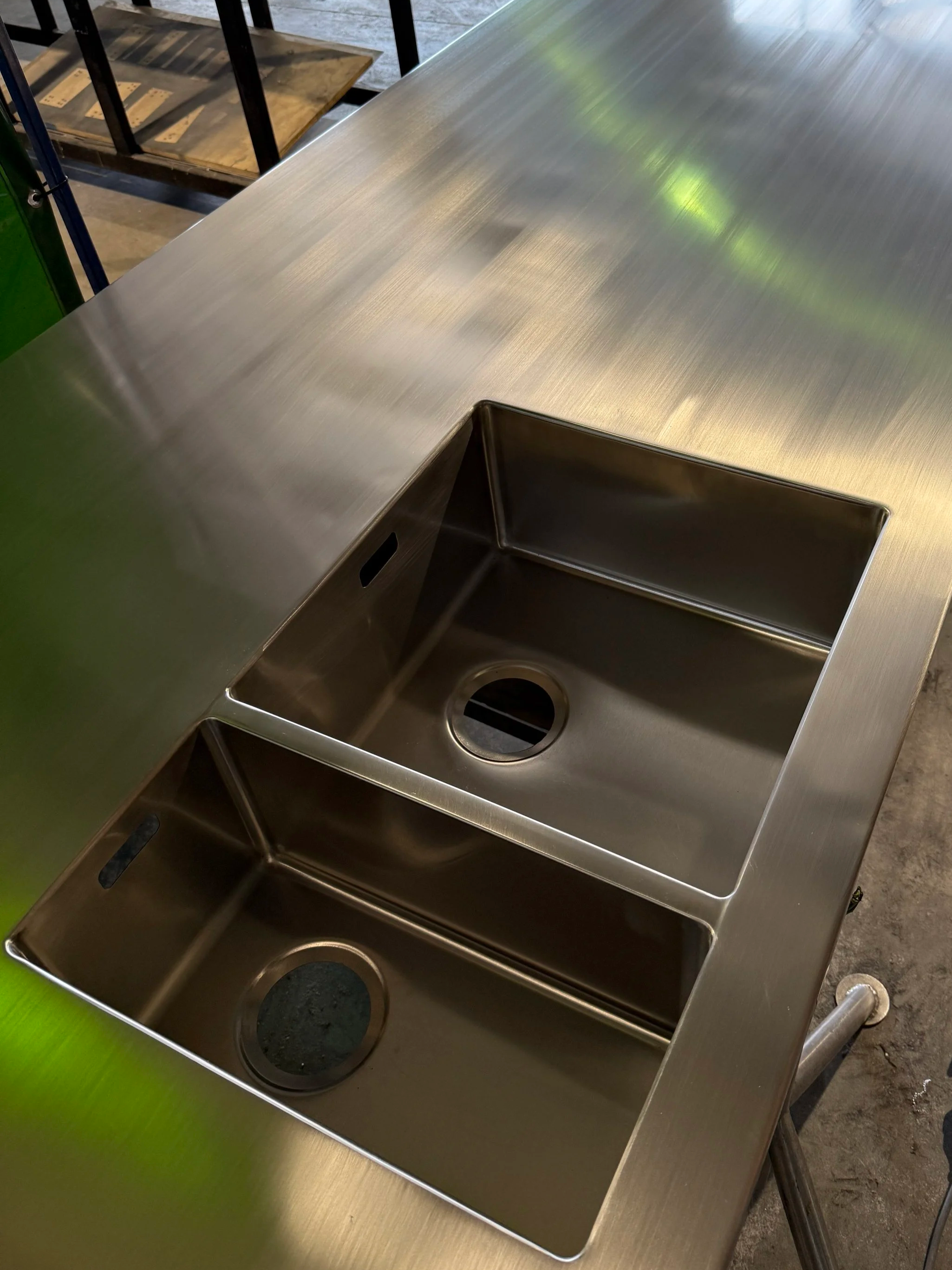 A stainless steel kitchen sink with a single basin and a drain at the bottom, set into a light-colored countertop.