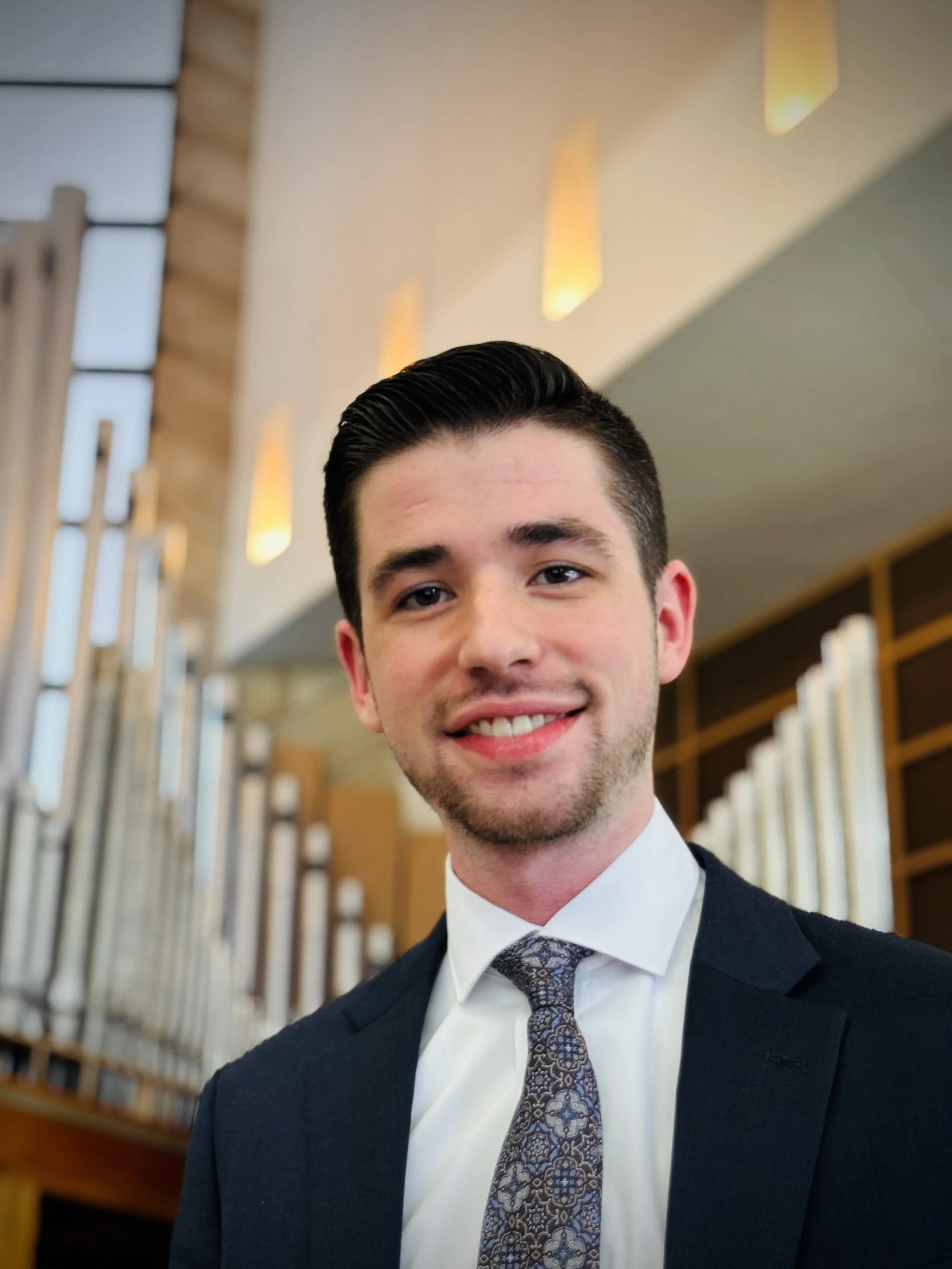 A young man in a suit and yellow tie taking a selfie inside a grand, ornate church with intricate gold and blue architectural details and stained glass windows.