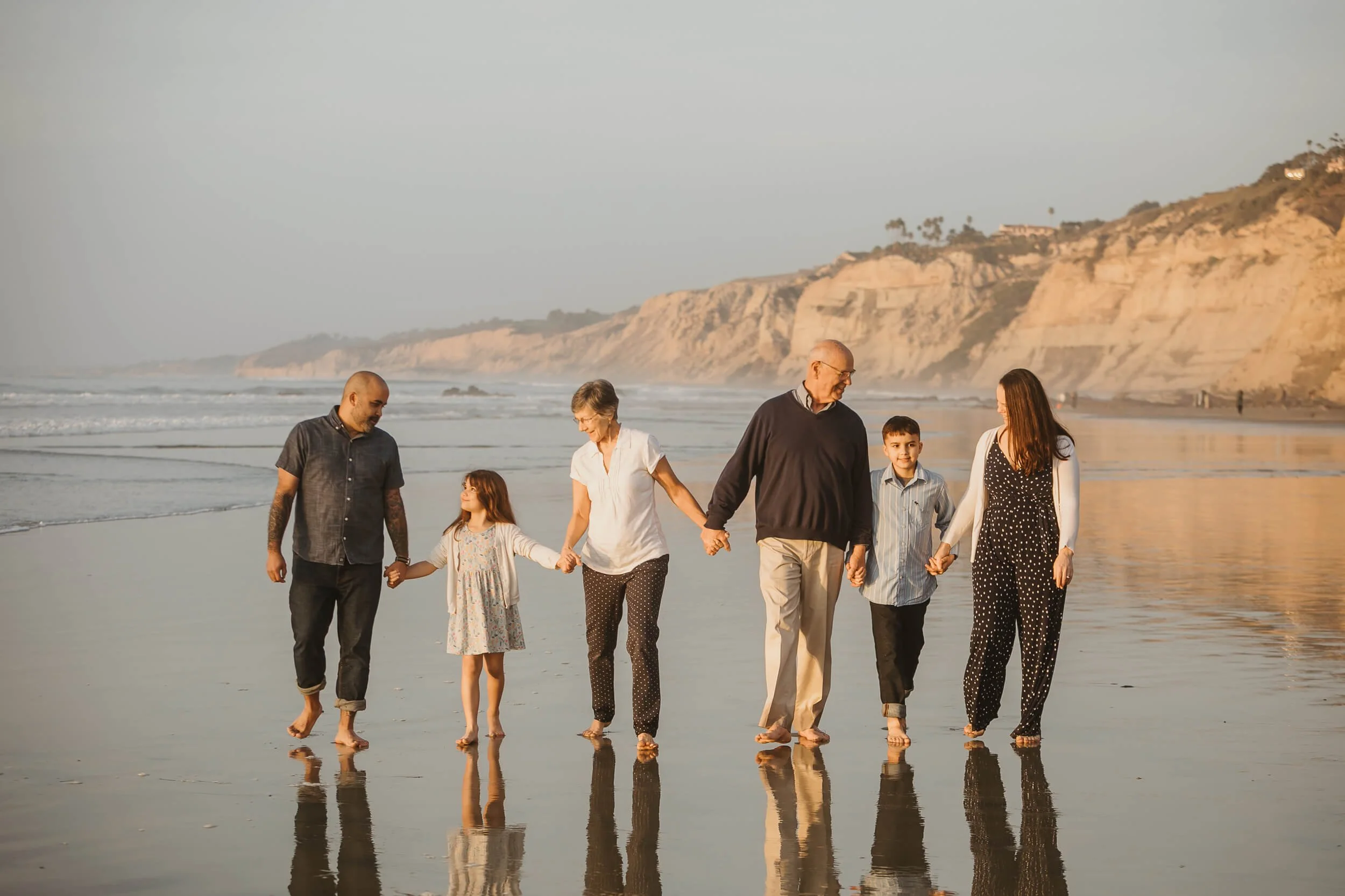 Large family walking on shoreline of La Jolla Shores with low tide and reflection in the sand for San Diego photography mini session