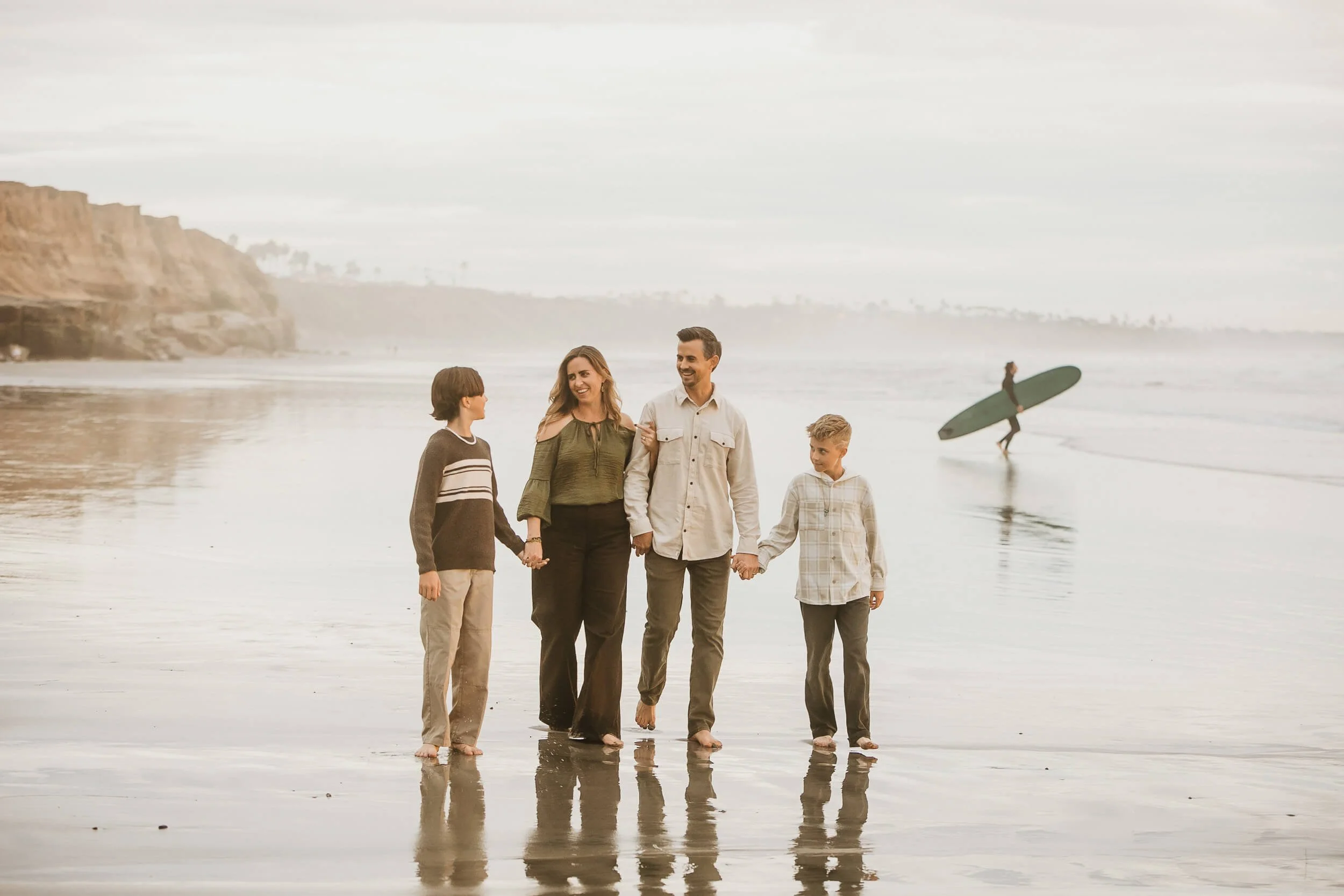 Family portrait with surfboard and ocean reflections during sunset in Carlsbad