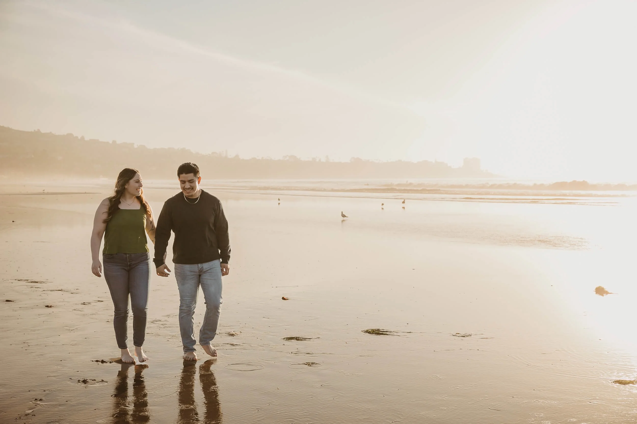 Casual photo of couple walking along beach looking at each other with La Jolla in the background diuring sunset 