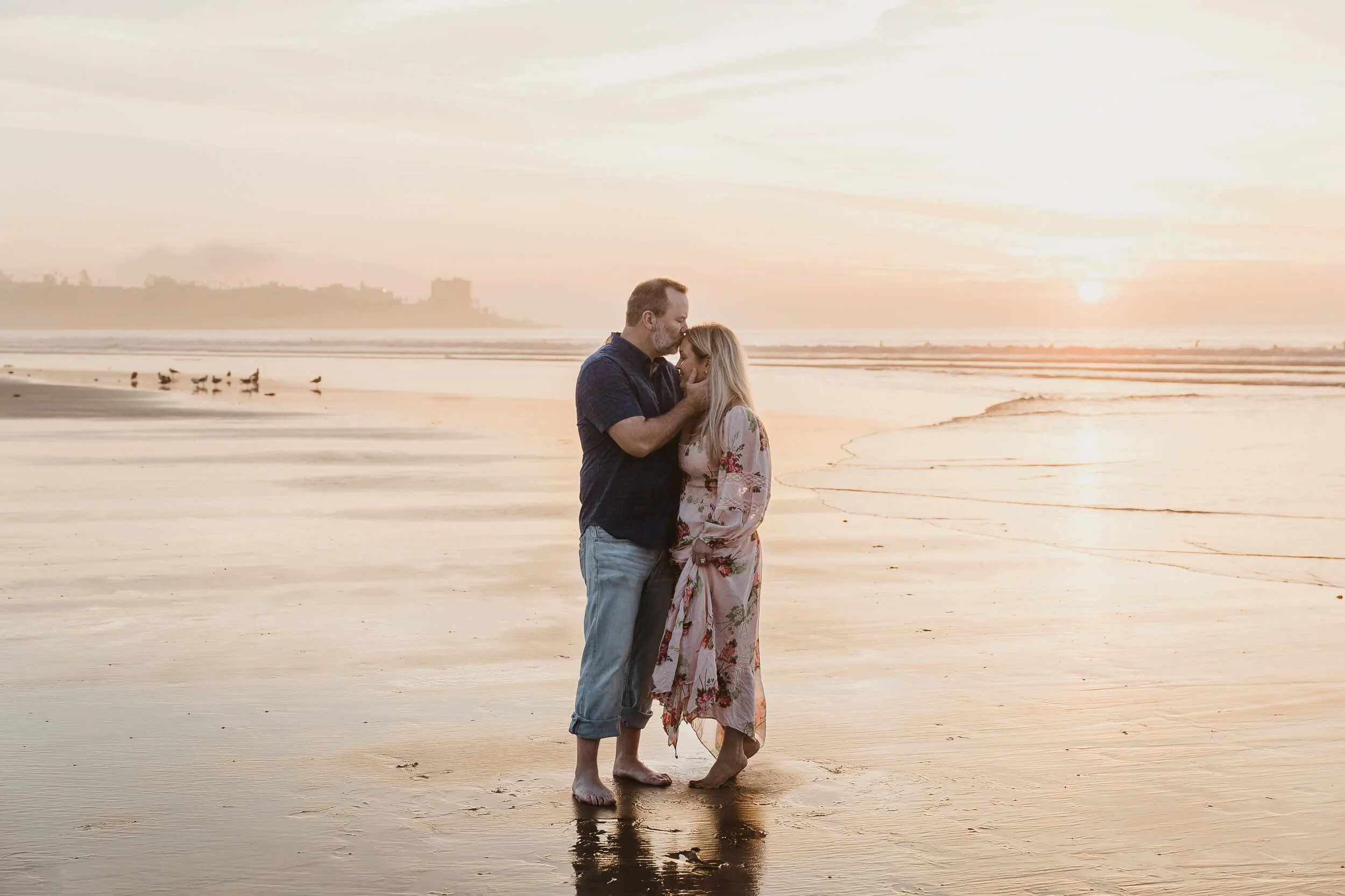 Man kissing wife's forehead with sun setting behind them at La Jolla Shores photo session golden hour