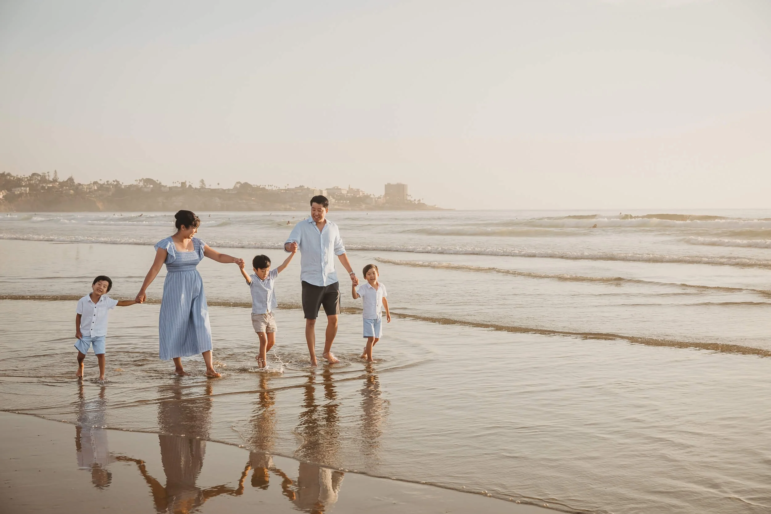 Candid family holding hands and walking along shoreline of La Jolla Shores for Scripps Pier photography session