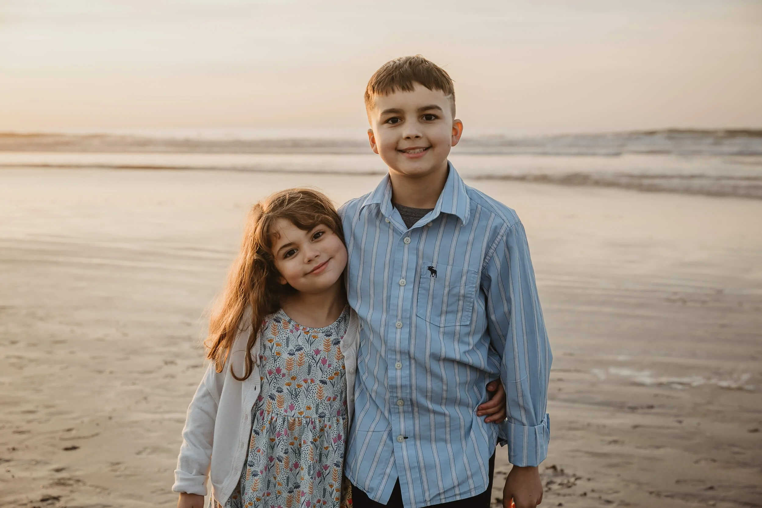Bother and sister posing for photo with a smile during golden hour at La Jolla Shores and Scripps Pier Family Photography in San Diego