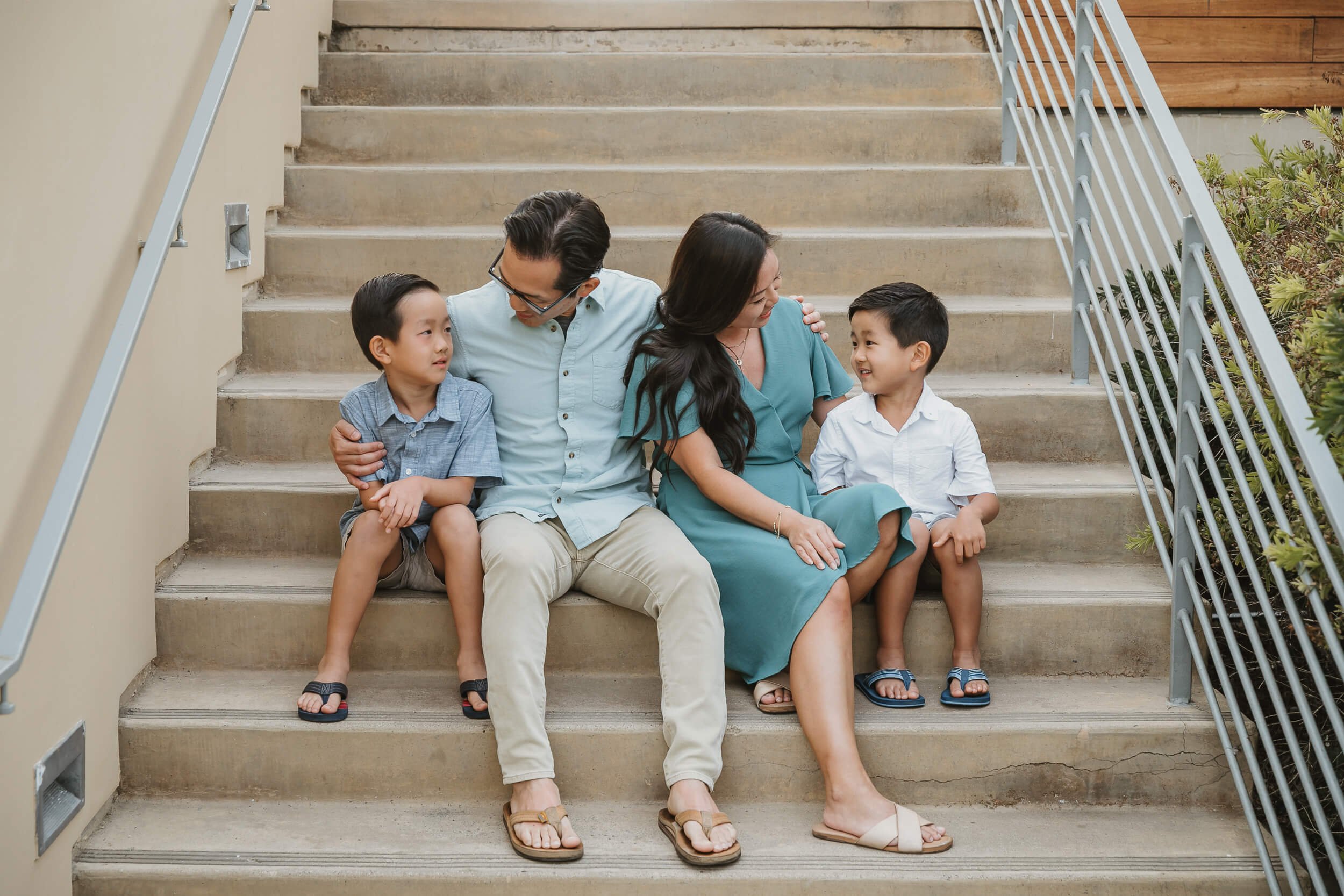 Candid family photo parents interacting with young toddlers sitting down stairs in La Jolla Seaside Forum for La Jolla Family session