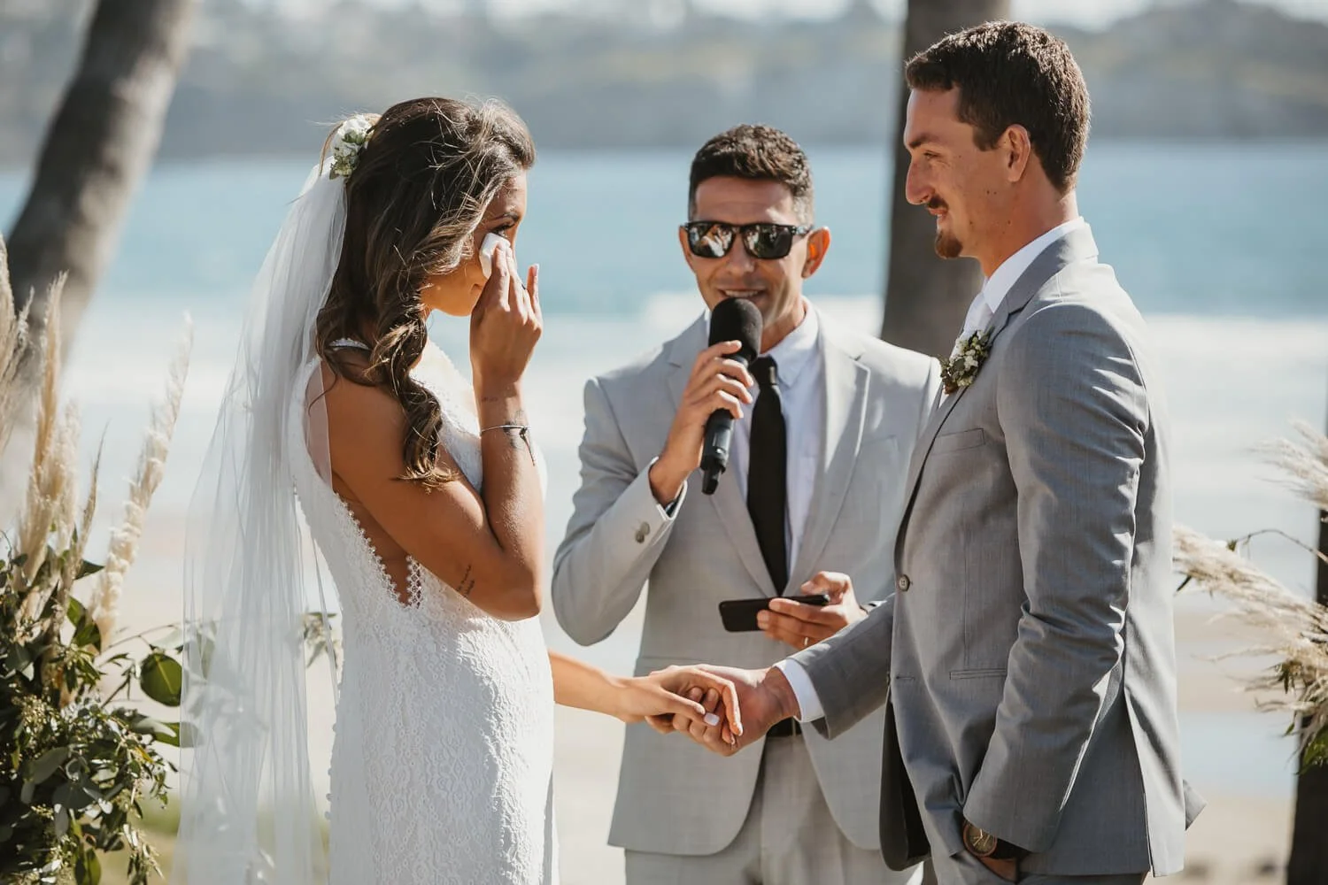 Bride wiping tears away during beachfront Scripps Seaside Forum wedding ceremony with palm trees