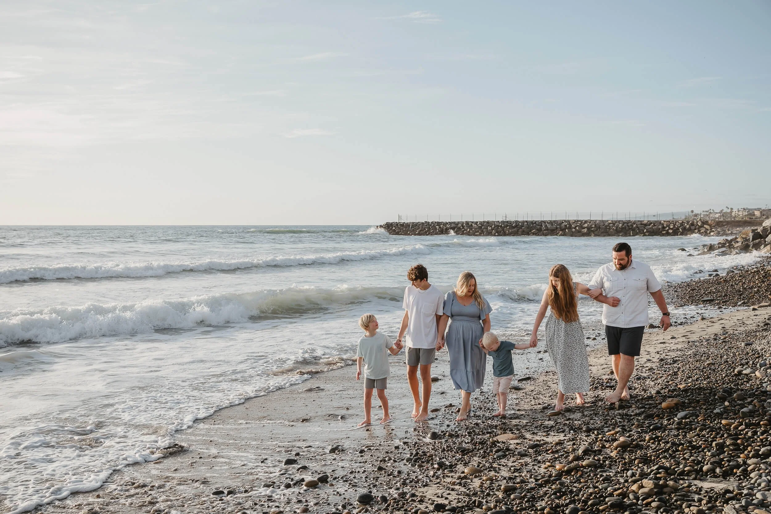 Candid family beach photography session with children playing near the waves in Carlsbad