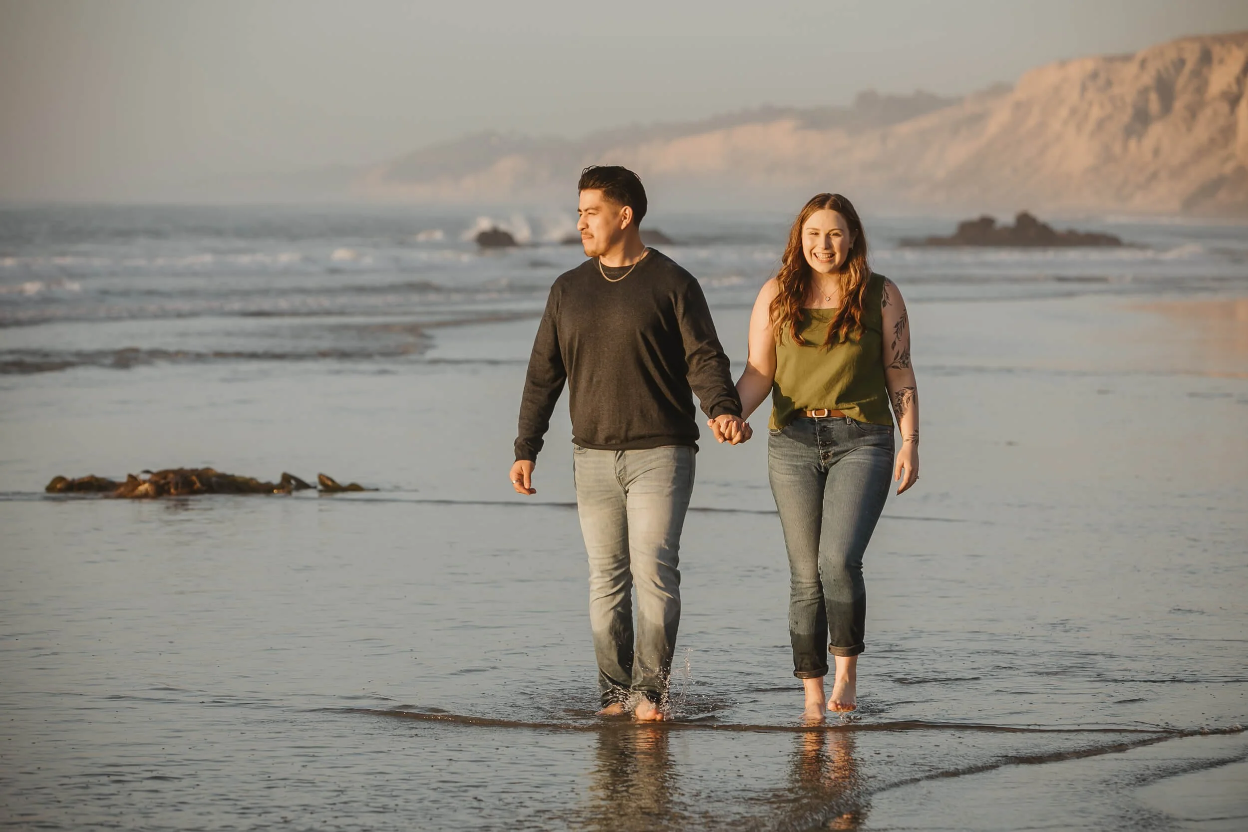 Couple having a good time walking and holding hands with tall cliffs and rocks exposed at La Jolla Session 