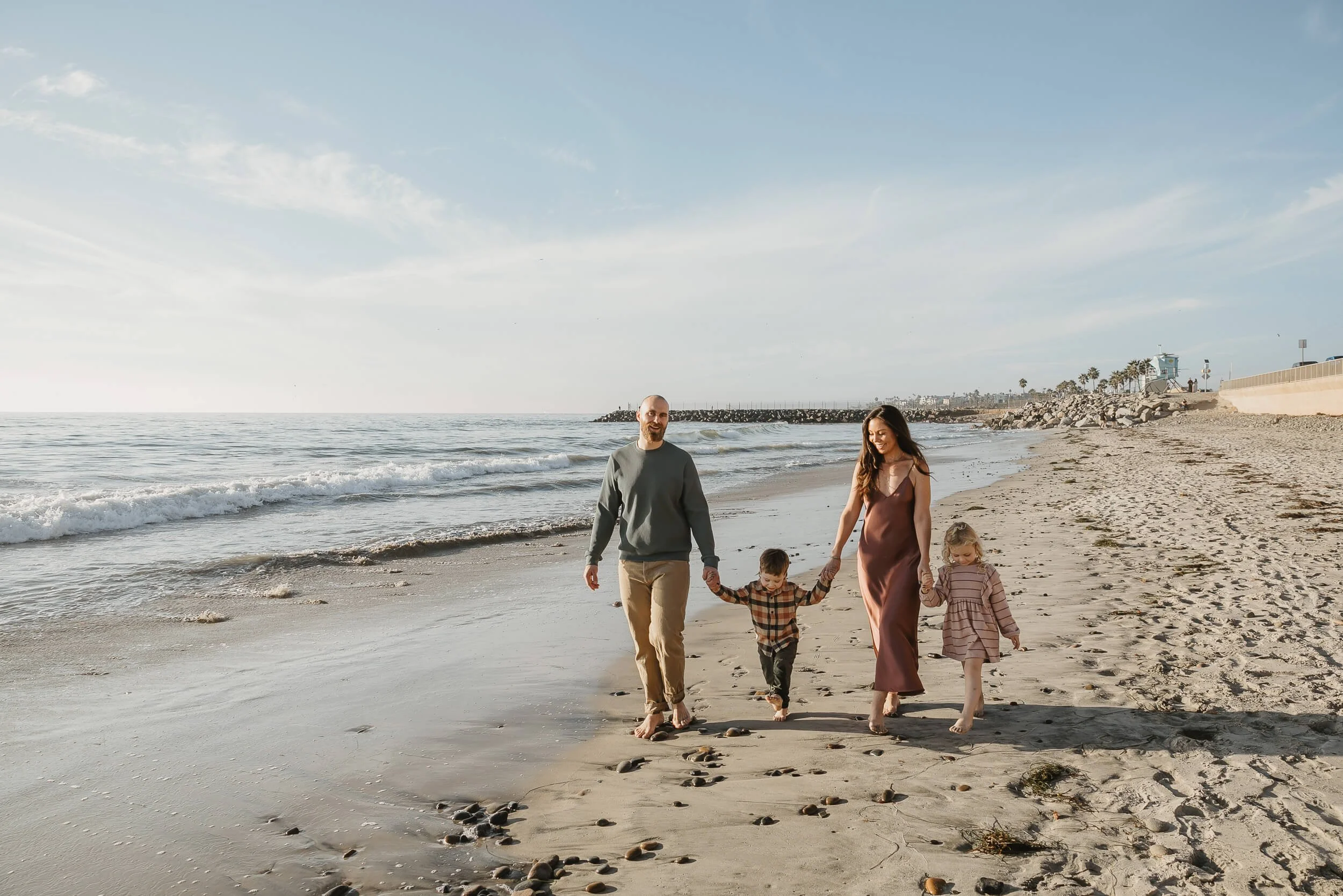 Candid beach family photography session with children walking by the water in Carlsbad