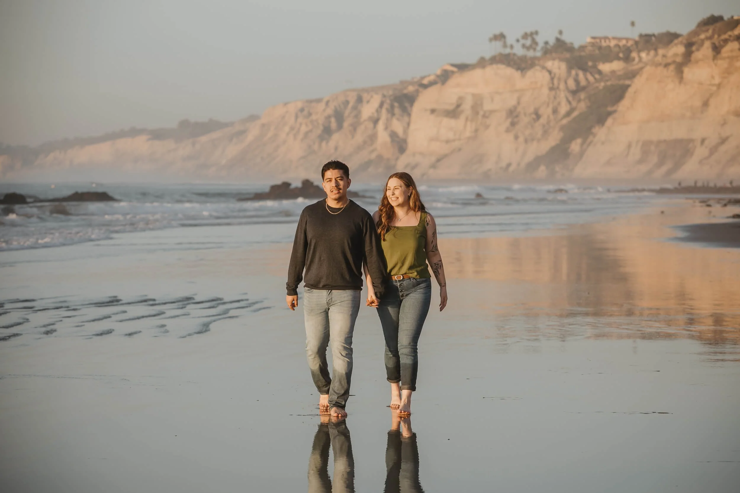 Casual couple walking on La Jolla Shores low tide shoreline, with Blacks Beach tall cliffs behind