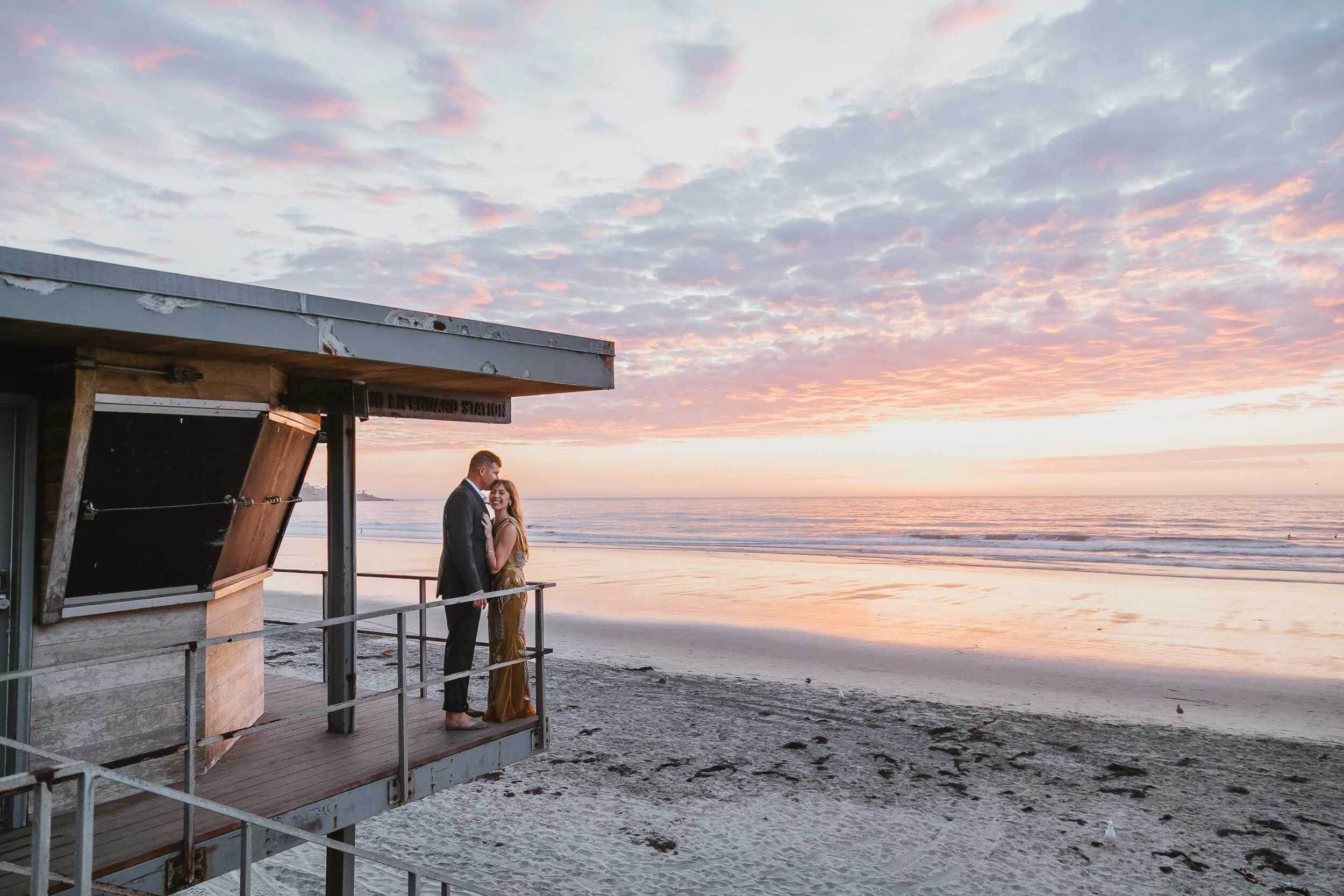 Couple on top of lifeguard tower during the sunset man kissing wife in forehead romantic San Diego mini session