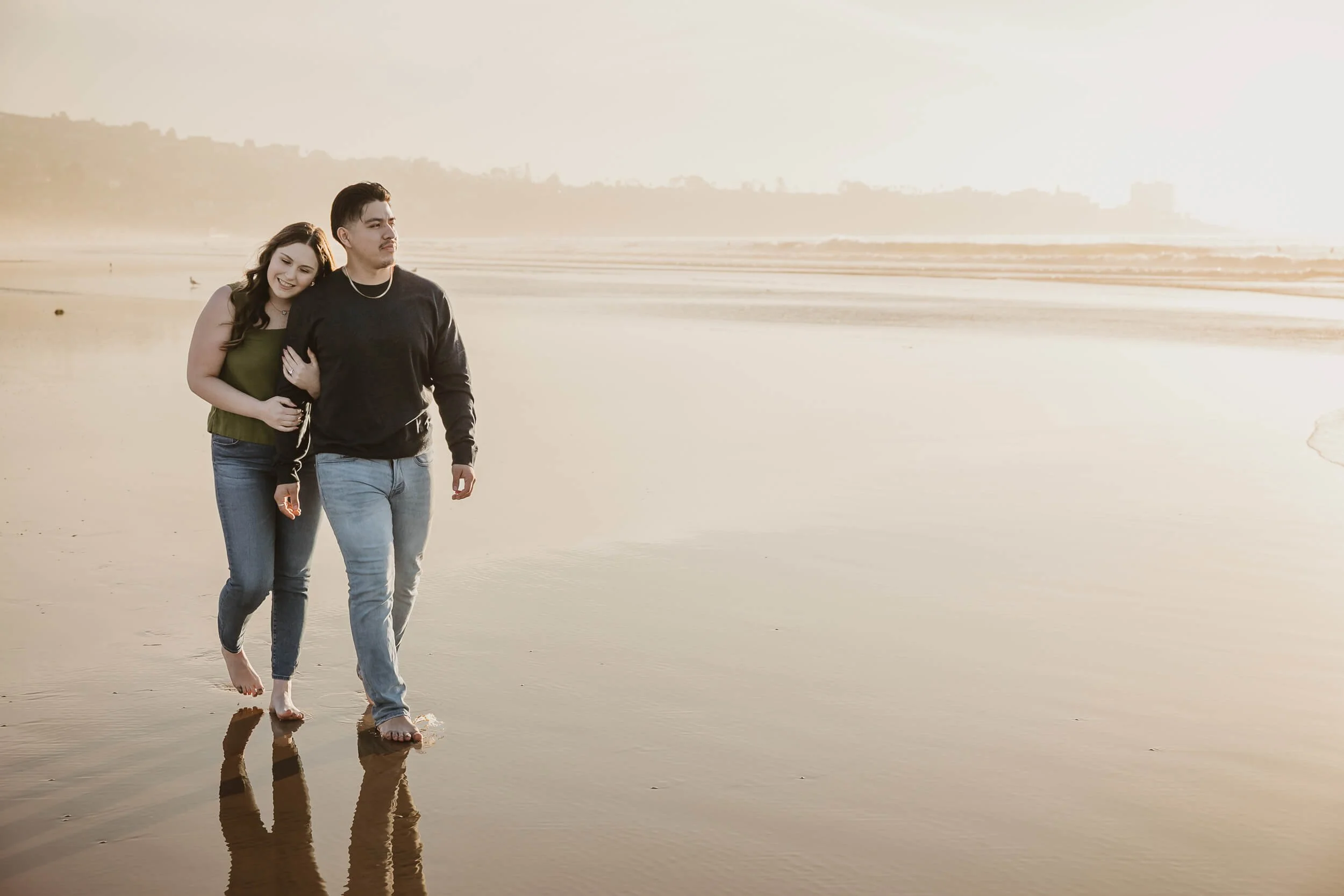 Woman laying head on man's shoulder while walking on the beach at La Jolla Shores during San Diego's golden hour