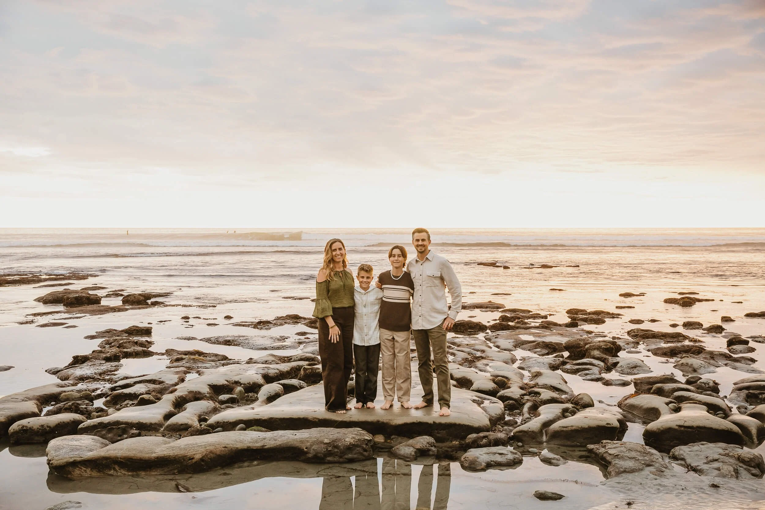 Family standing on tide pools during golden hour at the beach in Carlsbad, California