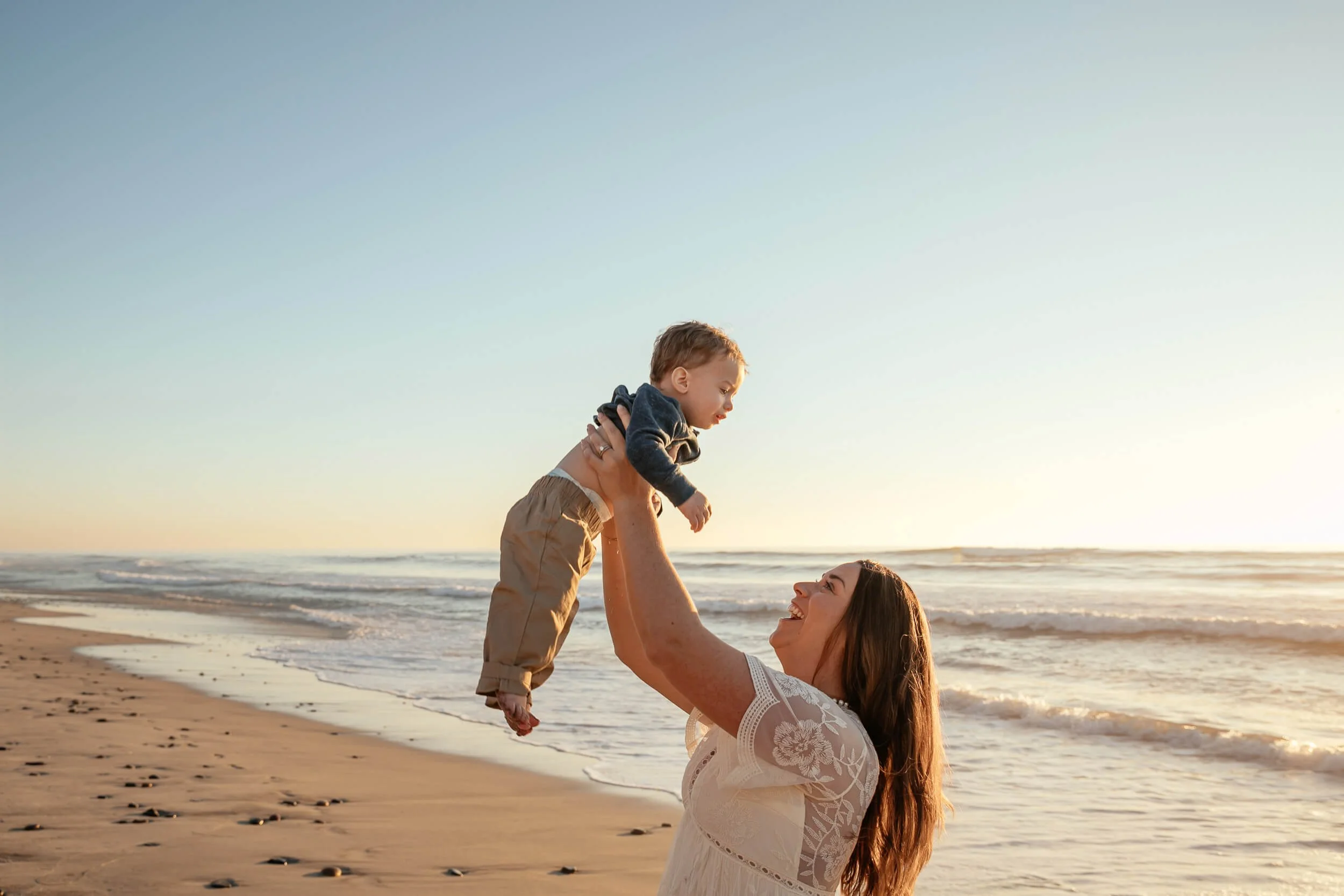 Mother lifting child at the beach during golden hour in Carlsbad, California