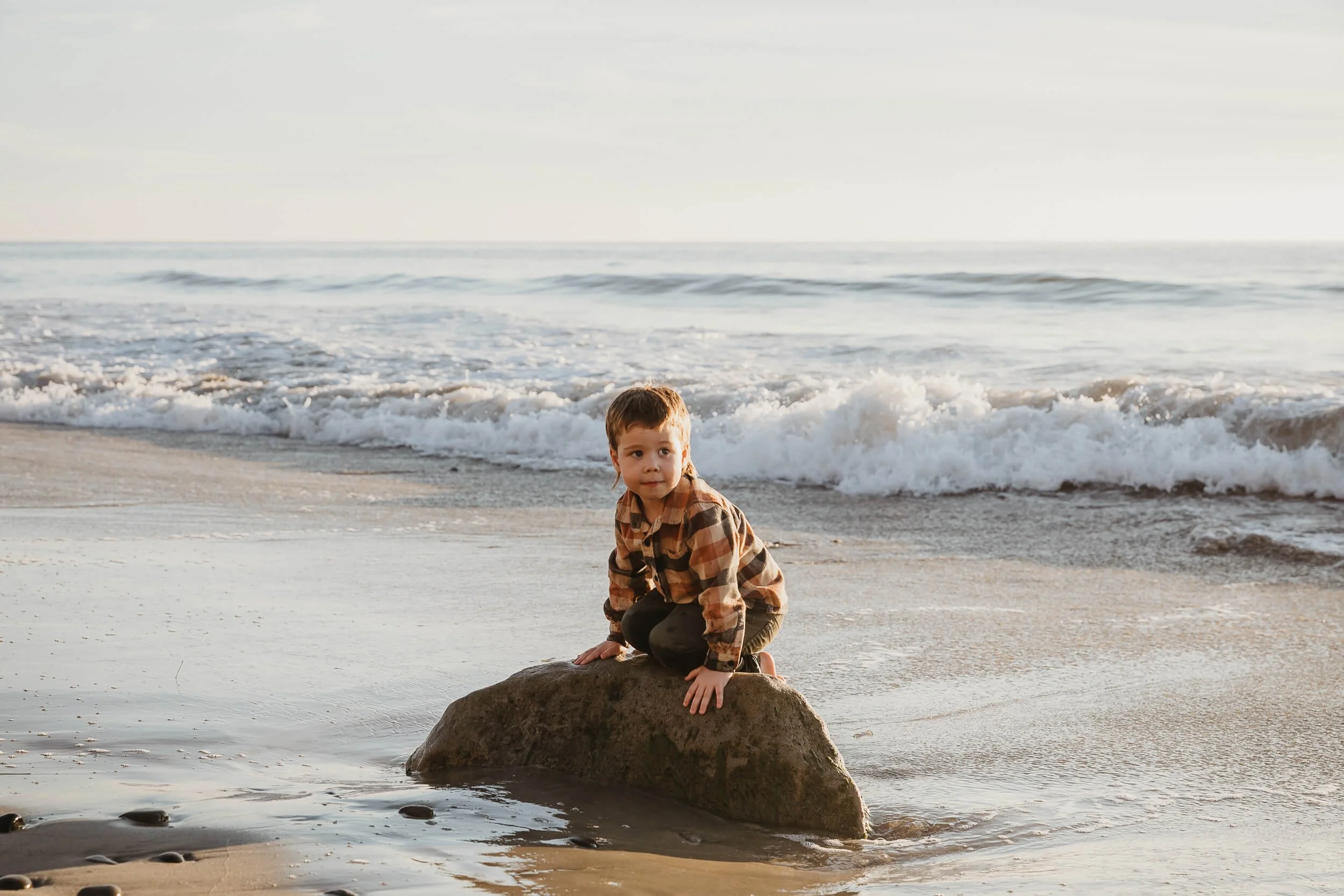 Child sitting on a rock by the ocean during a beach photography session in Carlsbad, California