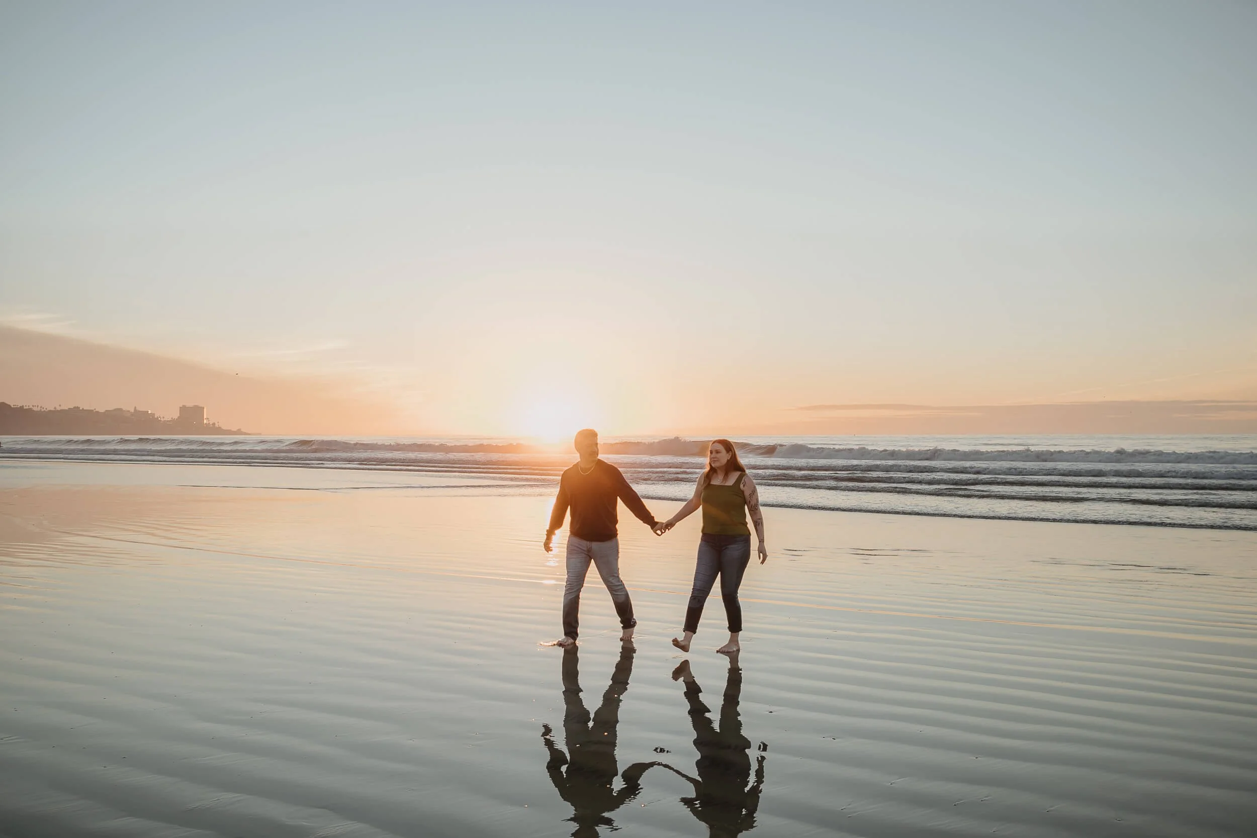 Wide photo couple having fun and walking in La Jolla beach during the sunset and low tide with reflections in sand 