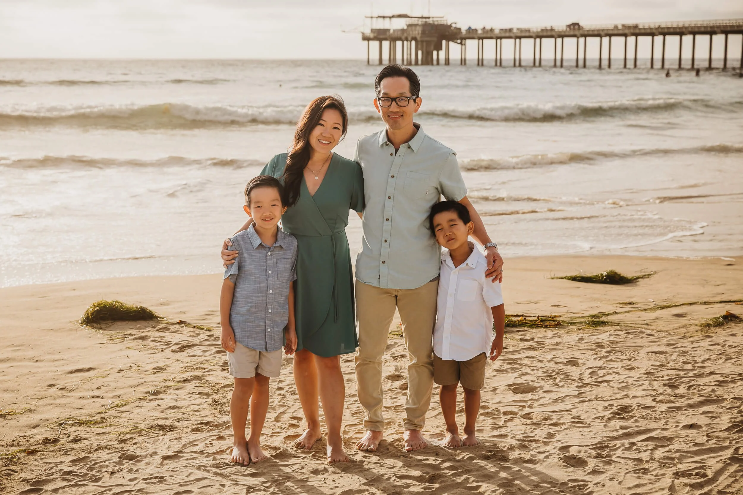 Family of four posing during San Diego family session in La Jolla Shores with Scripps Pier in background