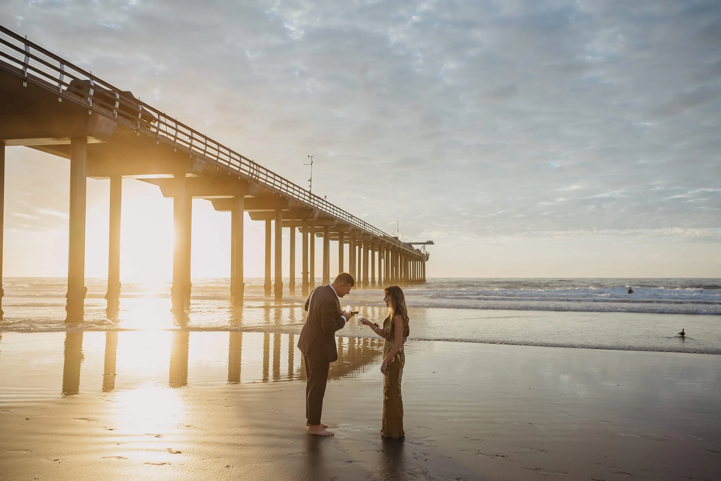 Man pouring Champagne for wife under the Scripps Pier on La Jolla Shore mini session 