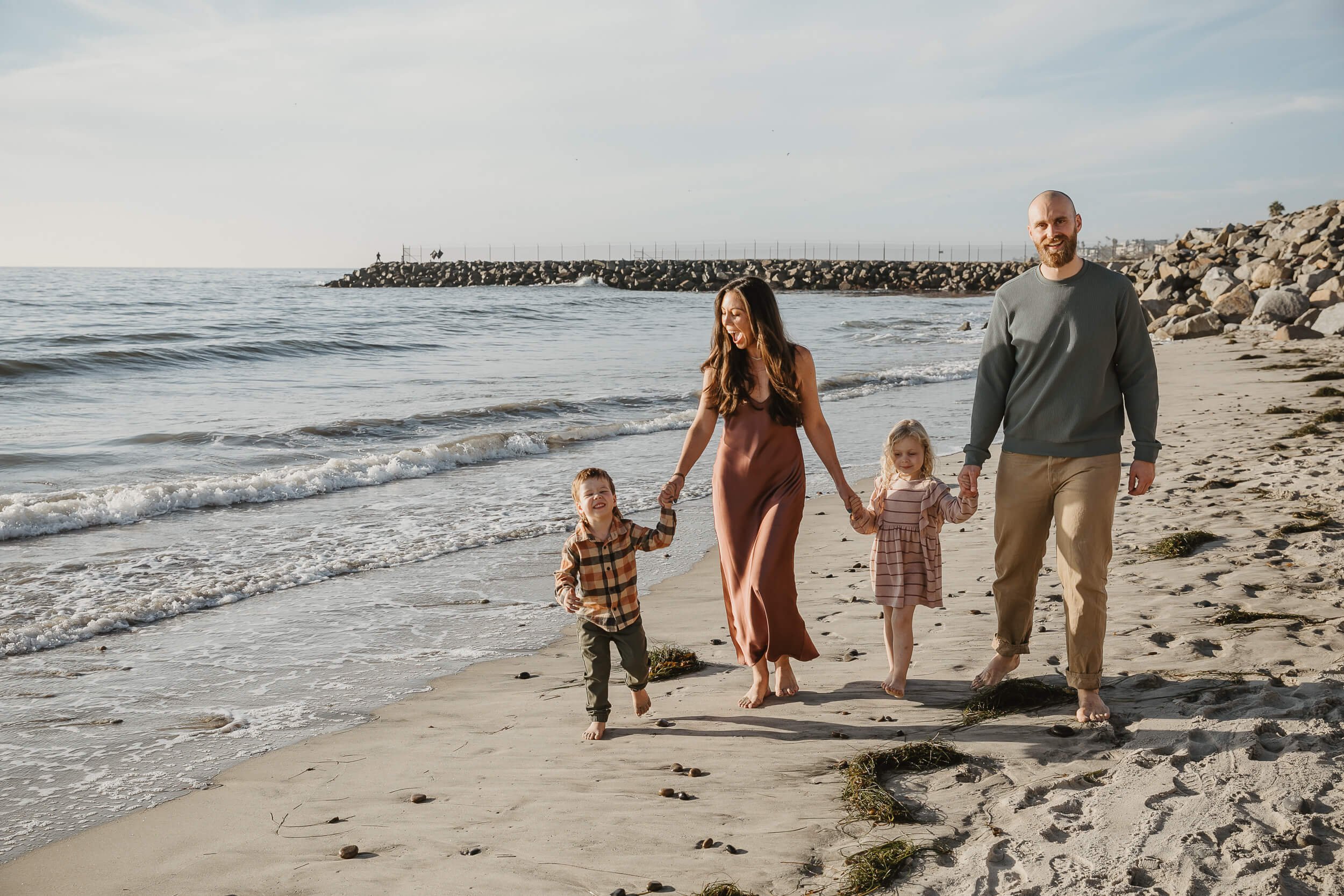 Family holding hands and walking on the beach at sunset in Carlsbad, California