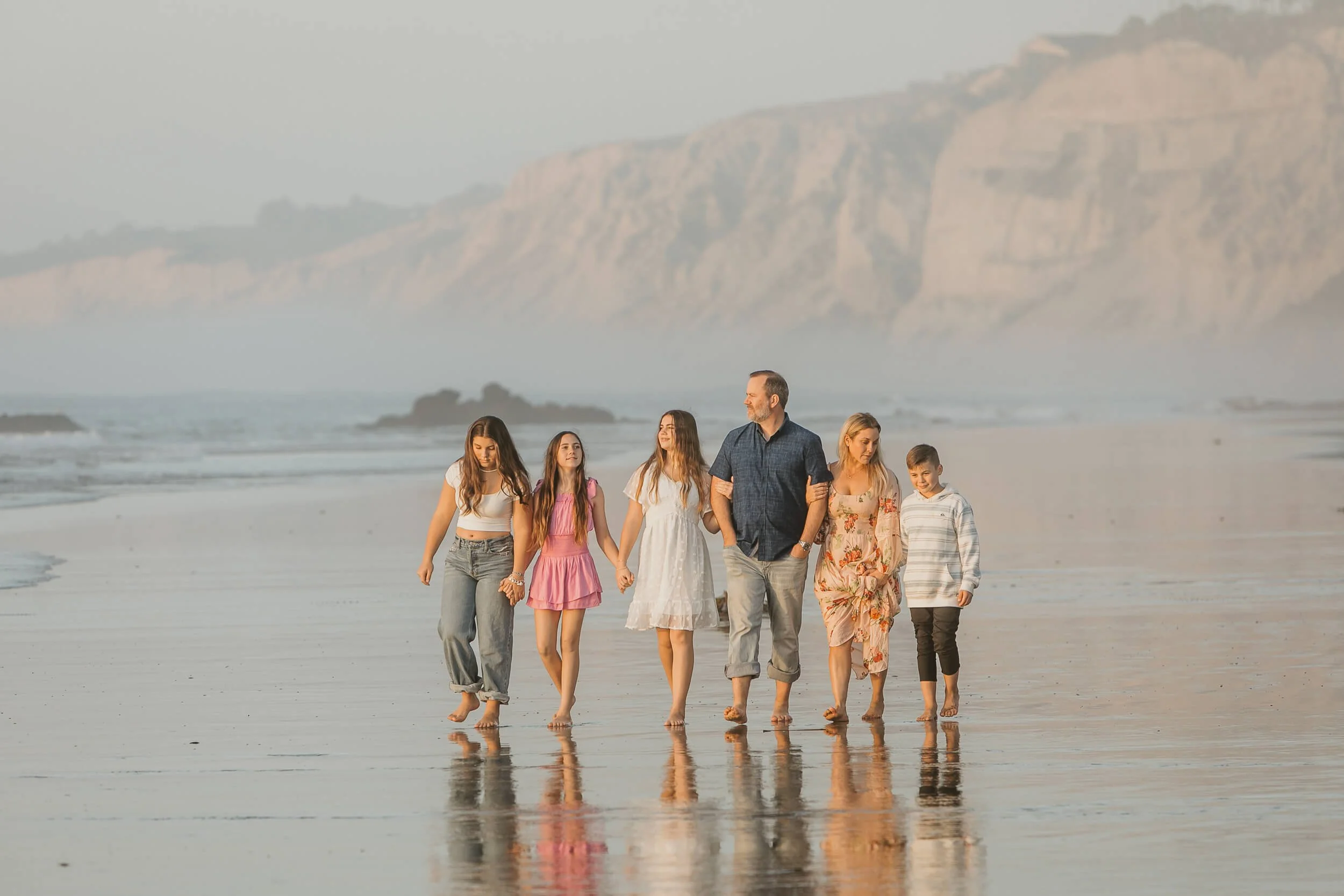 Candid family of six having fun while they walk on shoreline with cliffs behind during La Jolla Shores and Scripps Pier Family Photography in San Diego