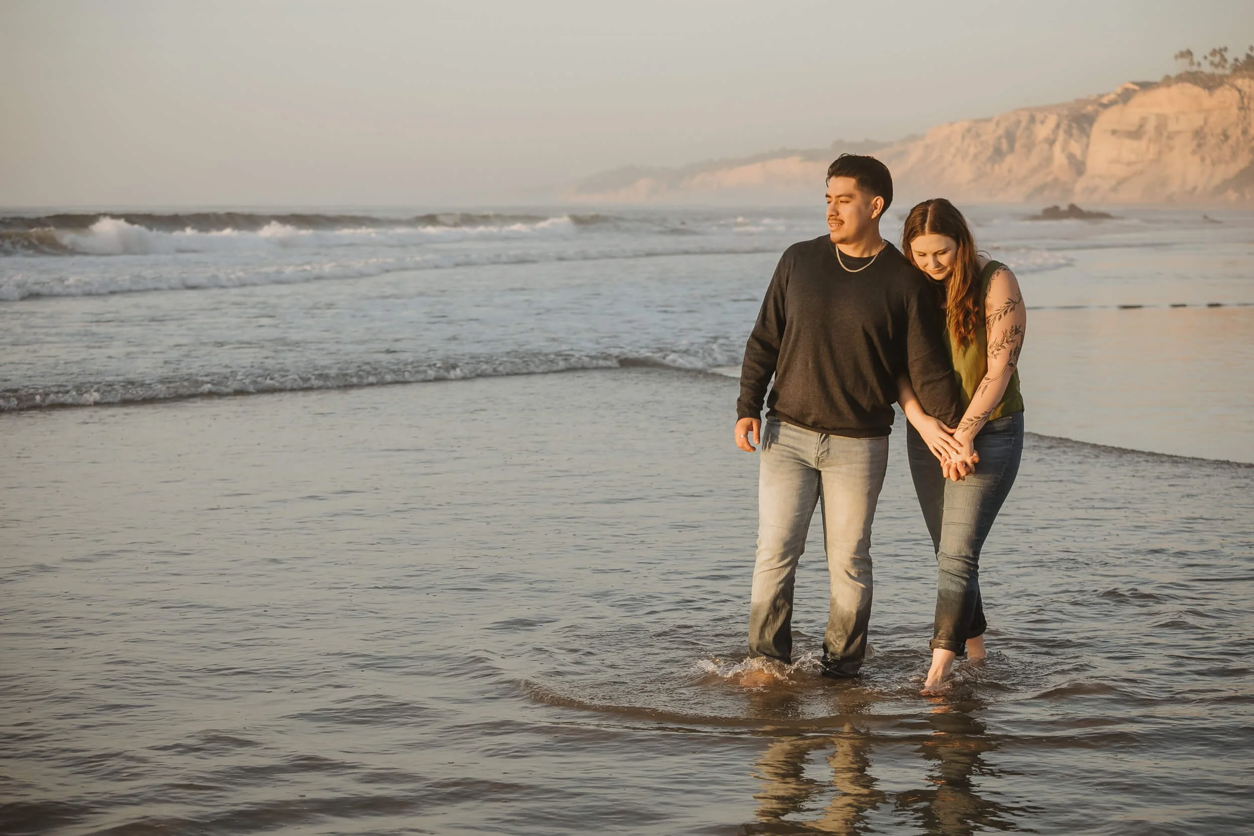 Couple walking on La Jolla Shores beach during sunset with their feet in water for romantic engagement session photo 