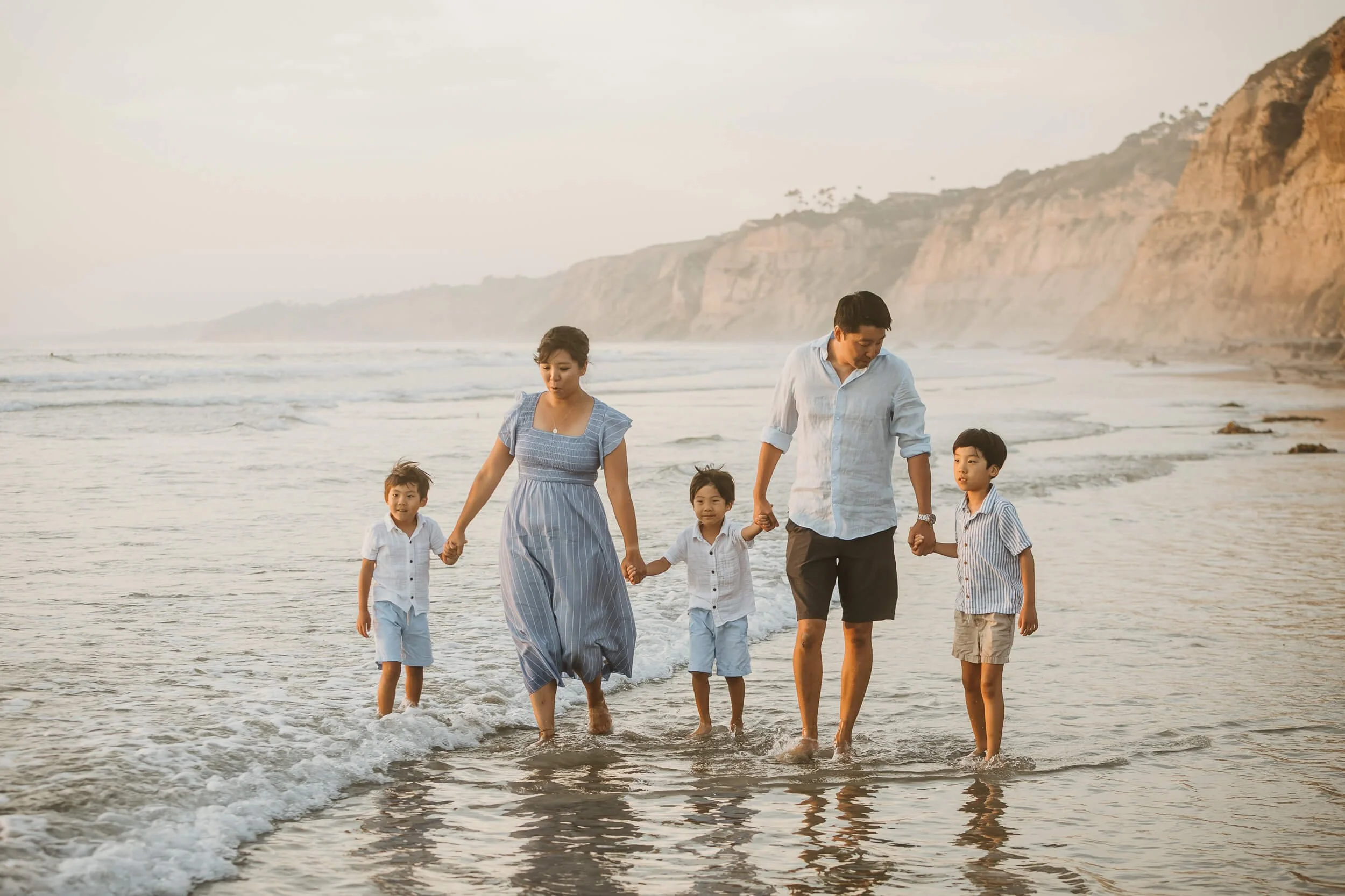 Candid shot parents and three boys walking along shoreline during San Diego family session in La Jolla Shores