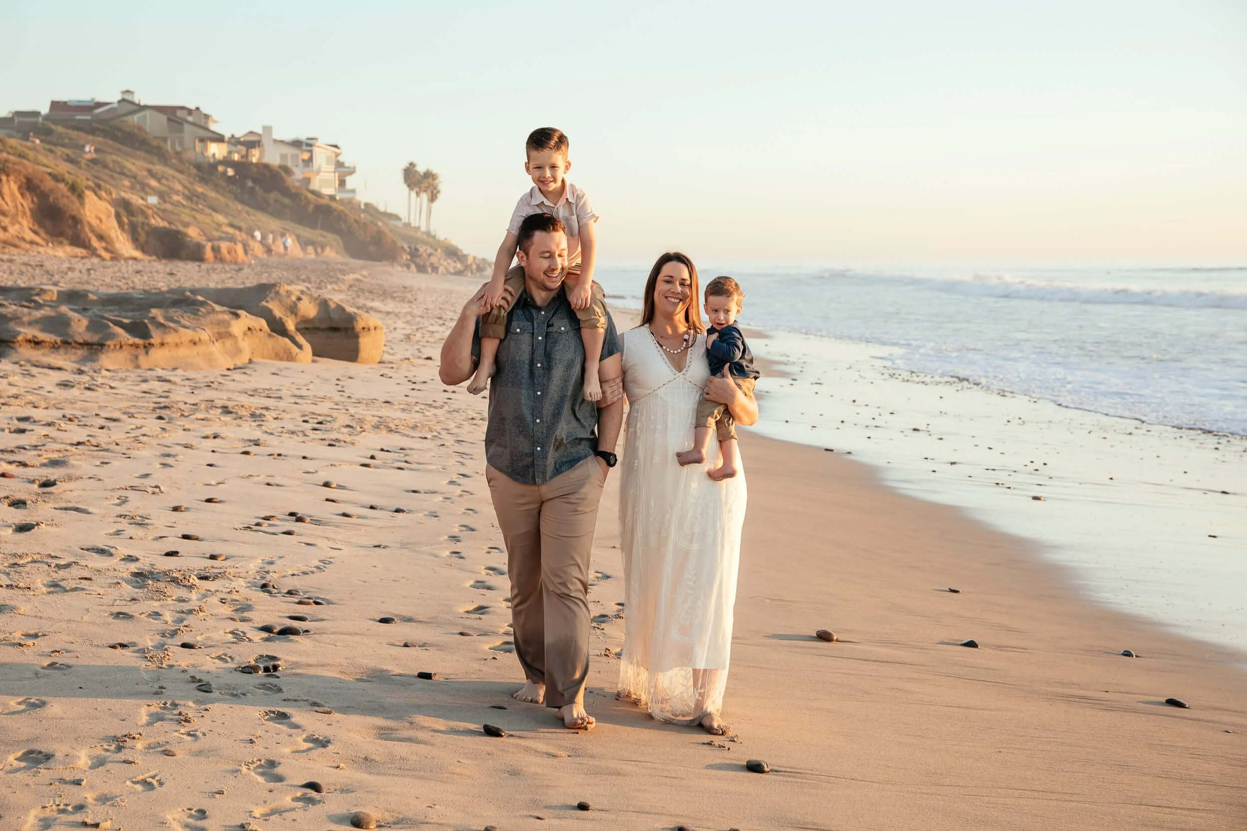 Beach family portrait with children riding on shoulders during sunset in Carlsbad