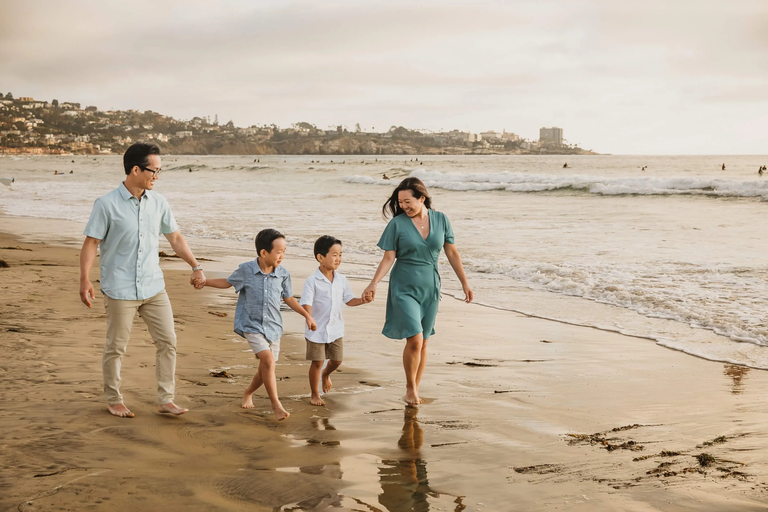 Happy family walking on shoreline of beach in La Jolla for San Diego family session during golden hour