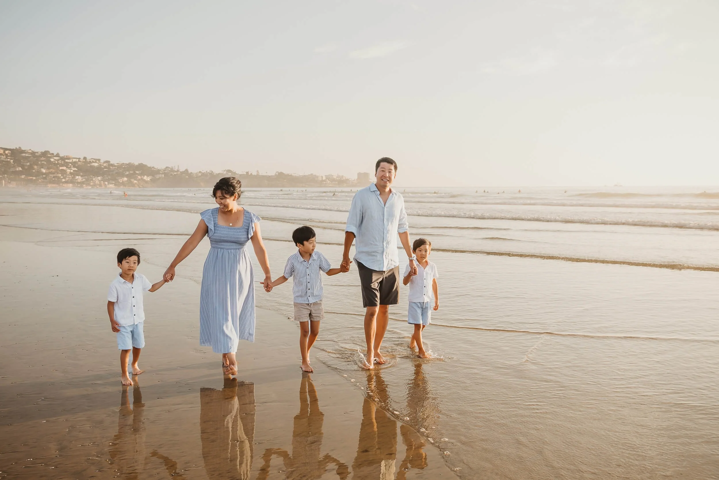 San Diego family session during golden hour parents and children walking along shoreline candid photograph