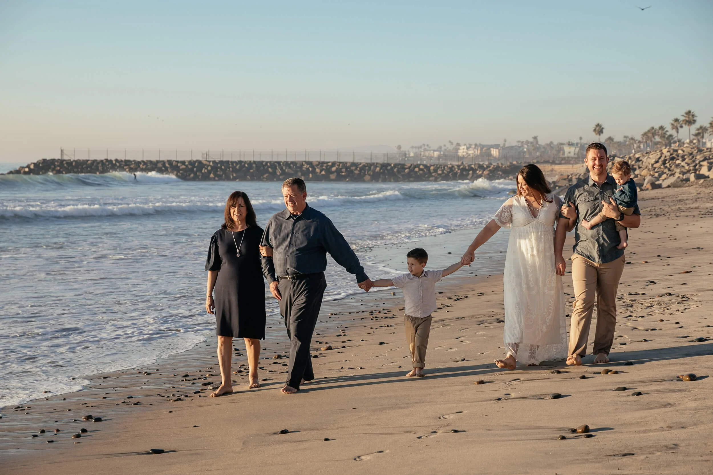 Family holding hands while walking along the shoreline in Carlsbad, California