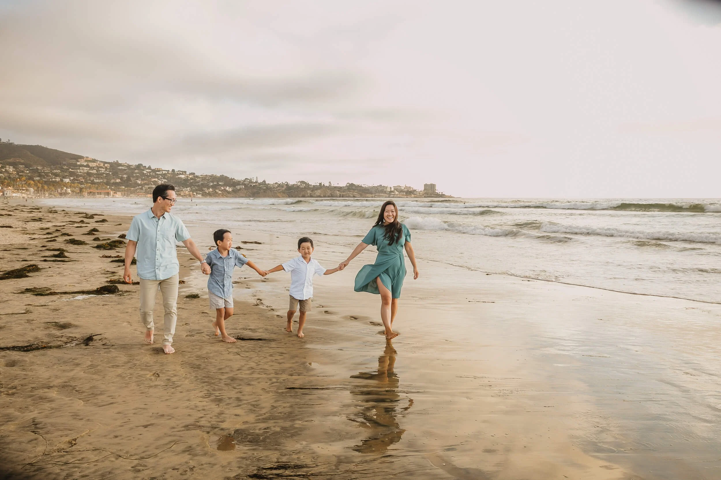 Wide shot family at beach holding hands during La Jolla Shores and Scripps Pier Family Photography in San Diego