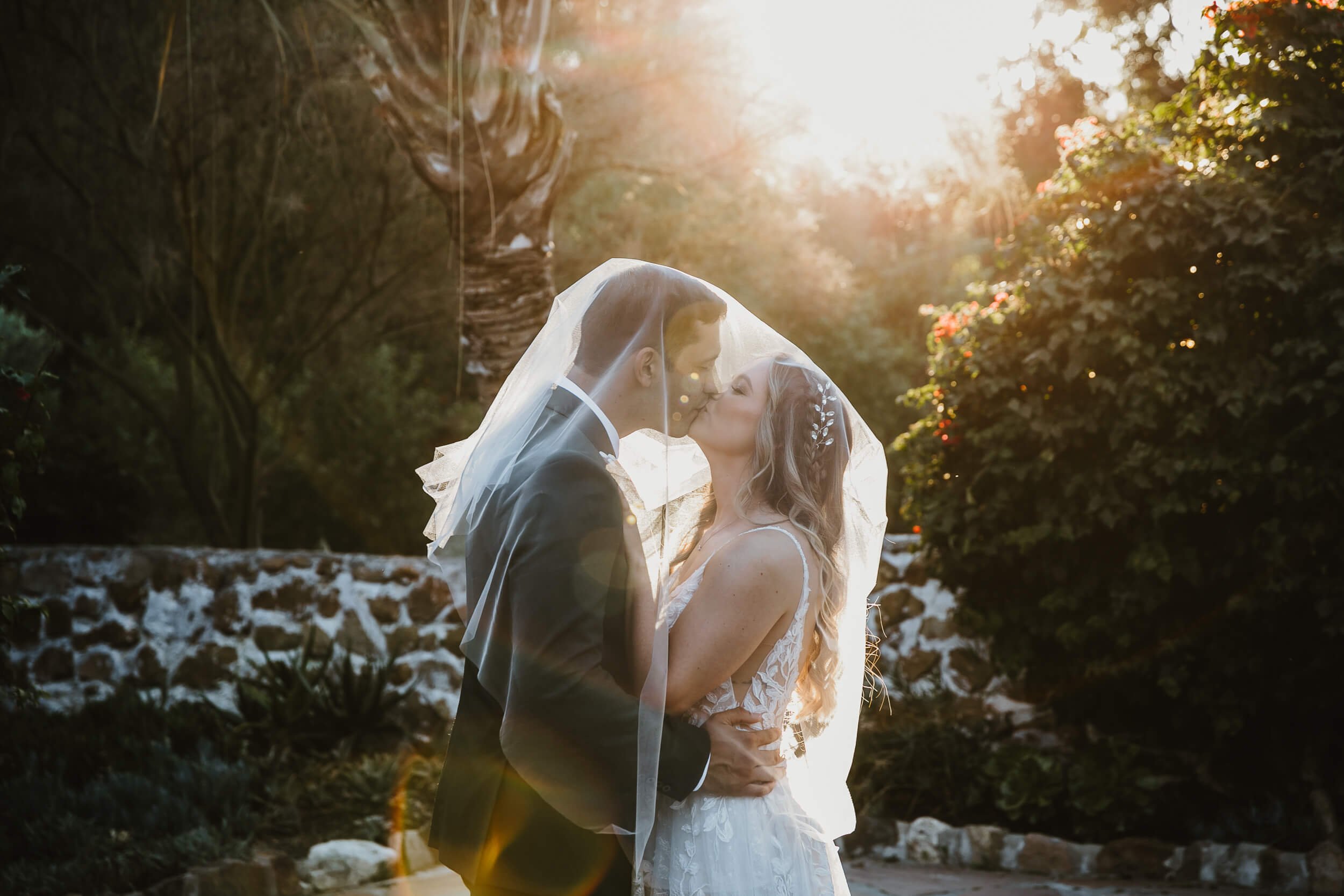 Backlit romantic moment bride and groom kissing under veil after Leo Carillo Ranch Wedding in Carlsbad