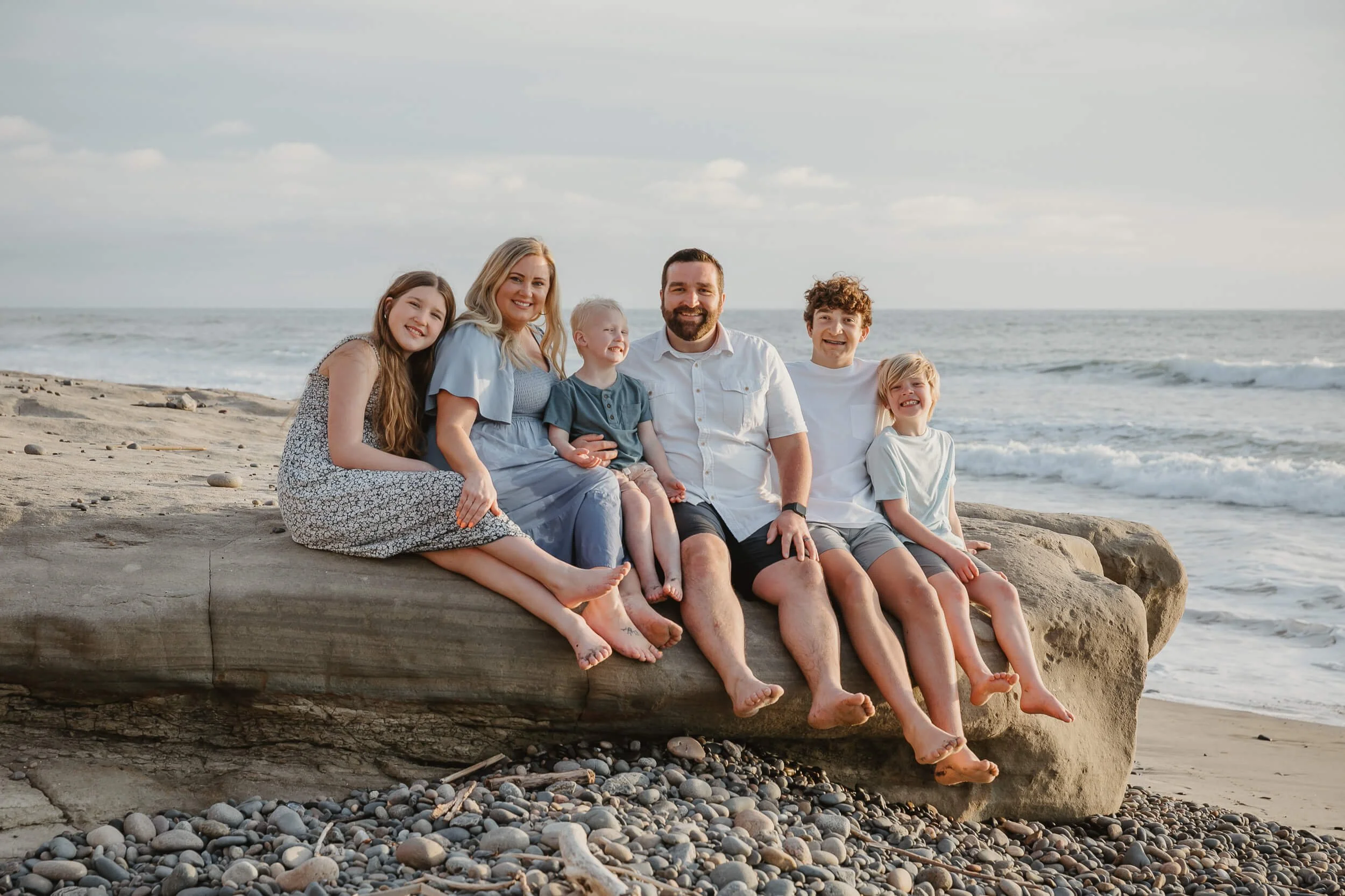 Relaxed family portrait sitting on driftwood at the beach in Carlsbad, California