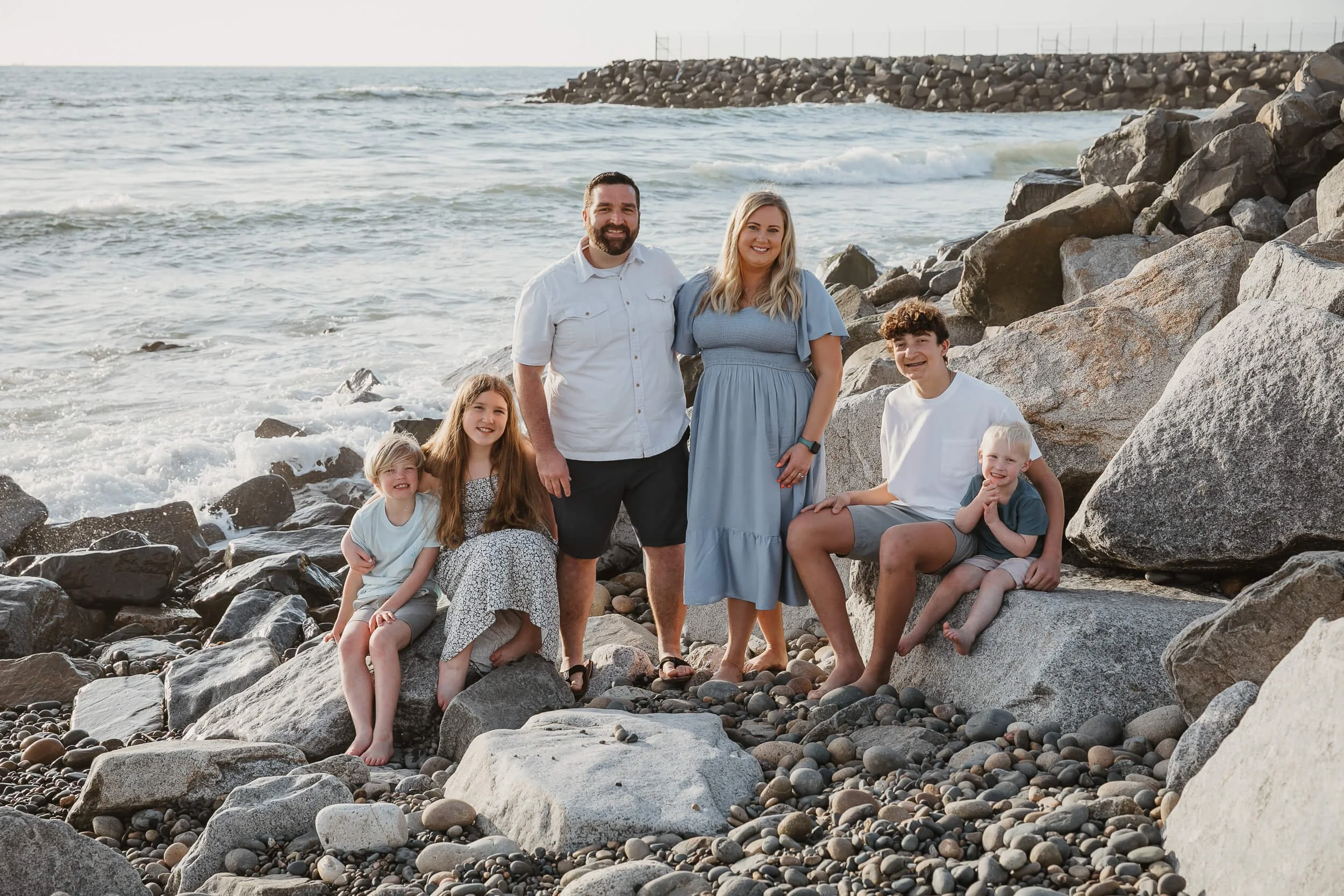 Large family portrait on beach rocks during golden hour photographed by a Carlsbad wedding photographer