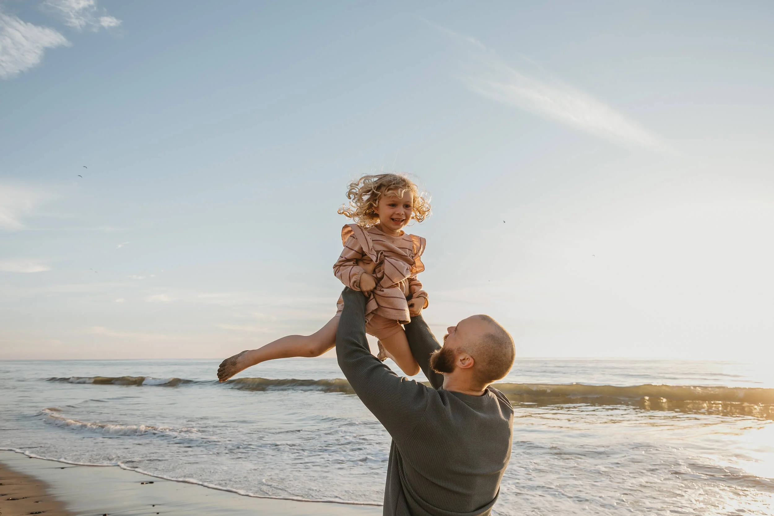 Father lifting daughter during a golden hour beach family photography session in Carlsbad