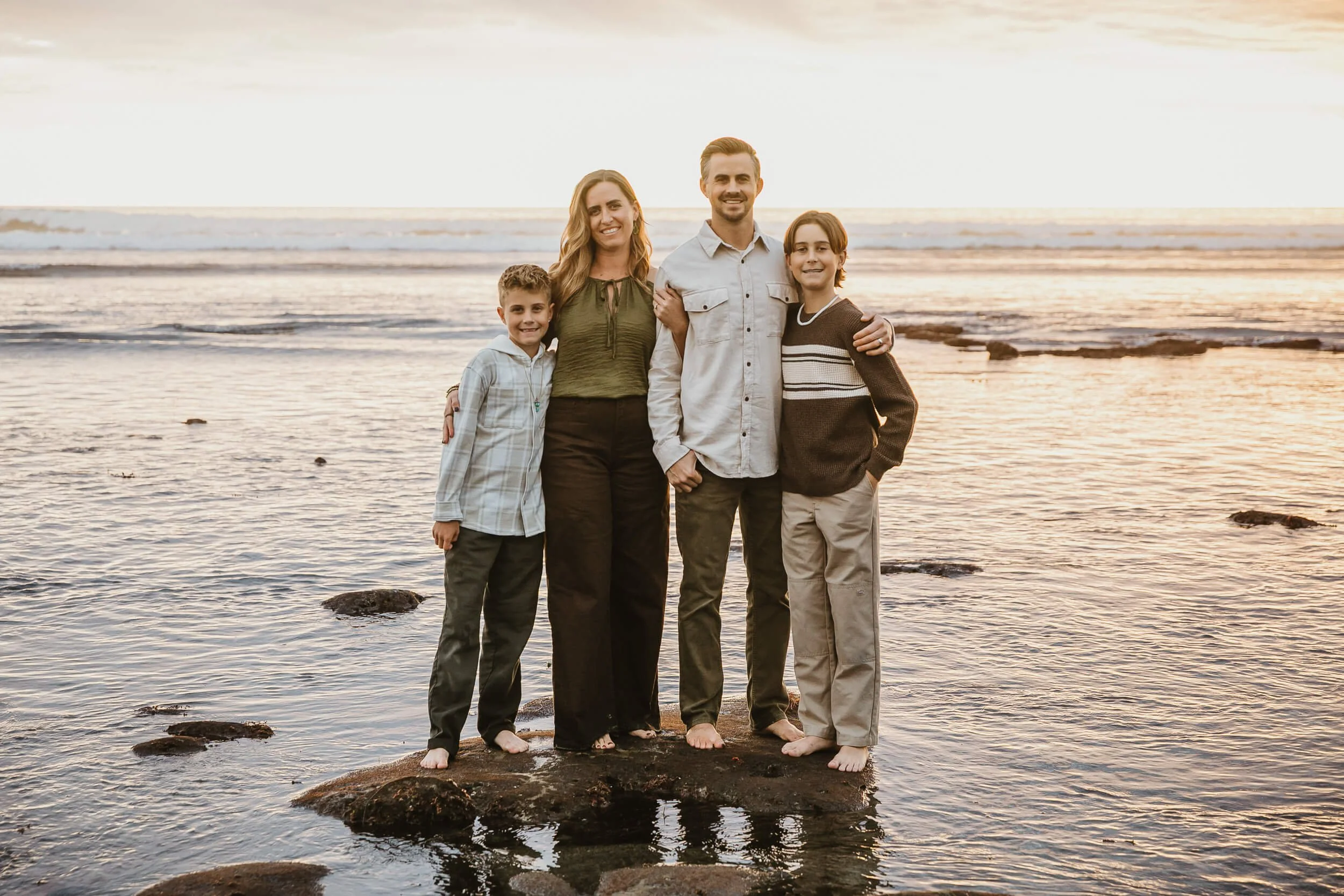 Family portrait on rocky shoreline during sunset photographed by a Carlsbad wedding photographer