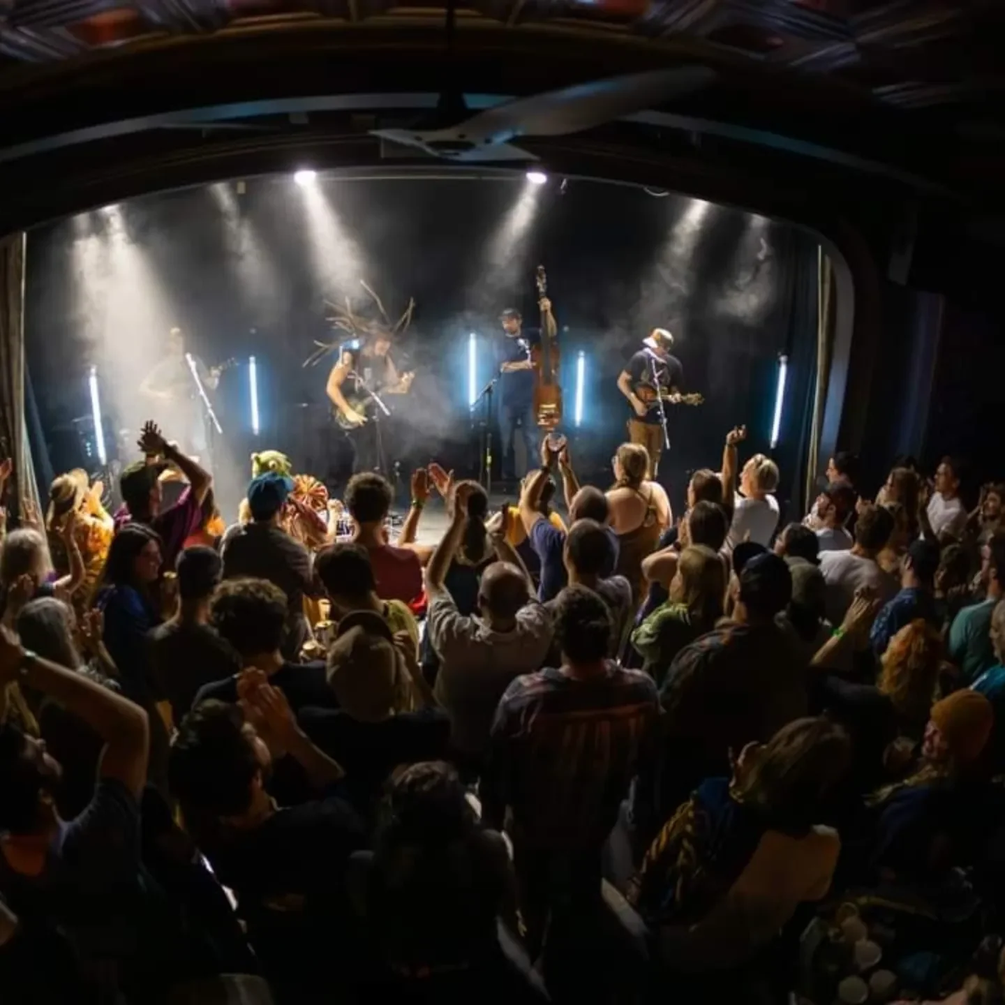 A band performing on stage with an audience enjoying the concert, some people are dancing and clapping.