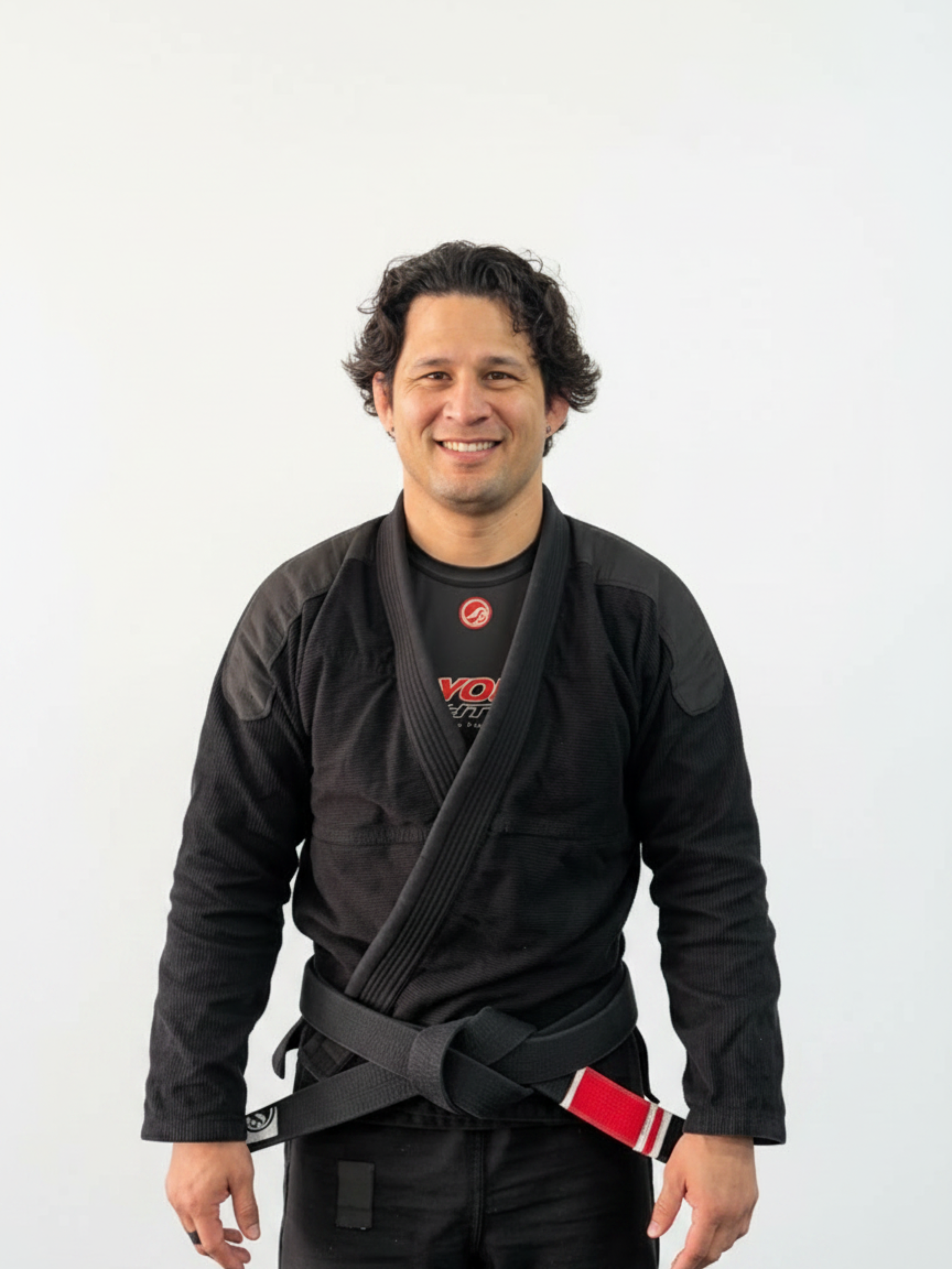 Man smiling, wearing cycling glasses and a black and white Checkmat cycling jersey, standing against a plain beige wall.
