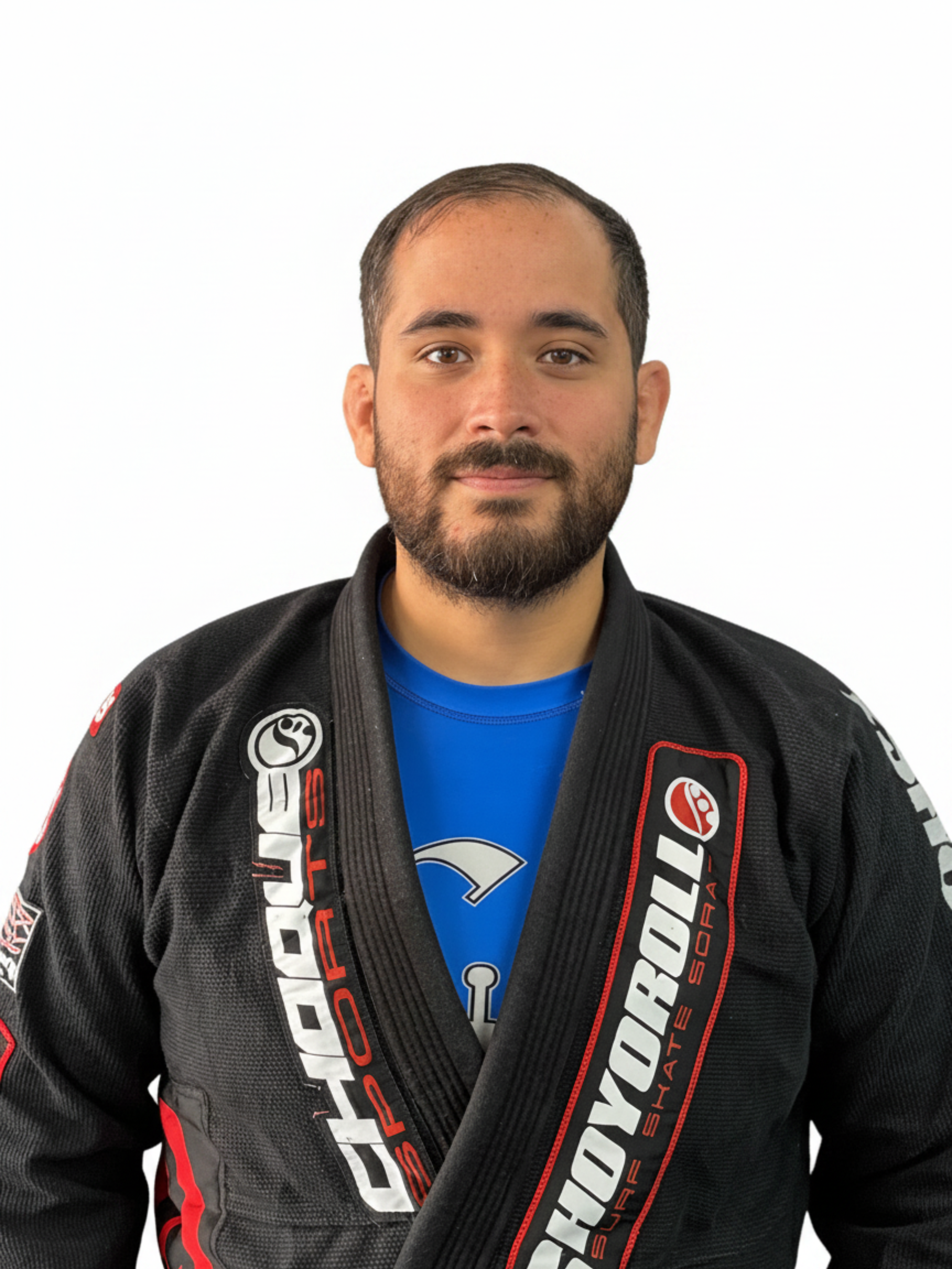 A man wearing a black Brazilian Jiu-Jitsu gi and a blue T-shirt, standing against a plain white background.