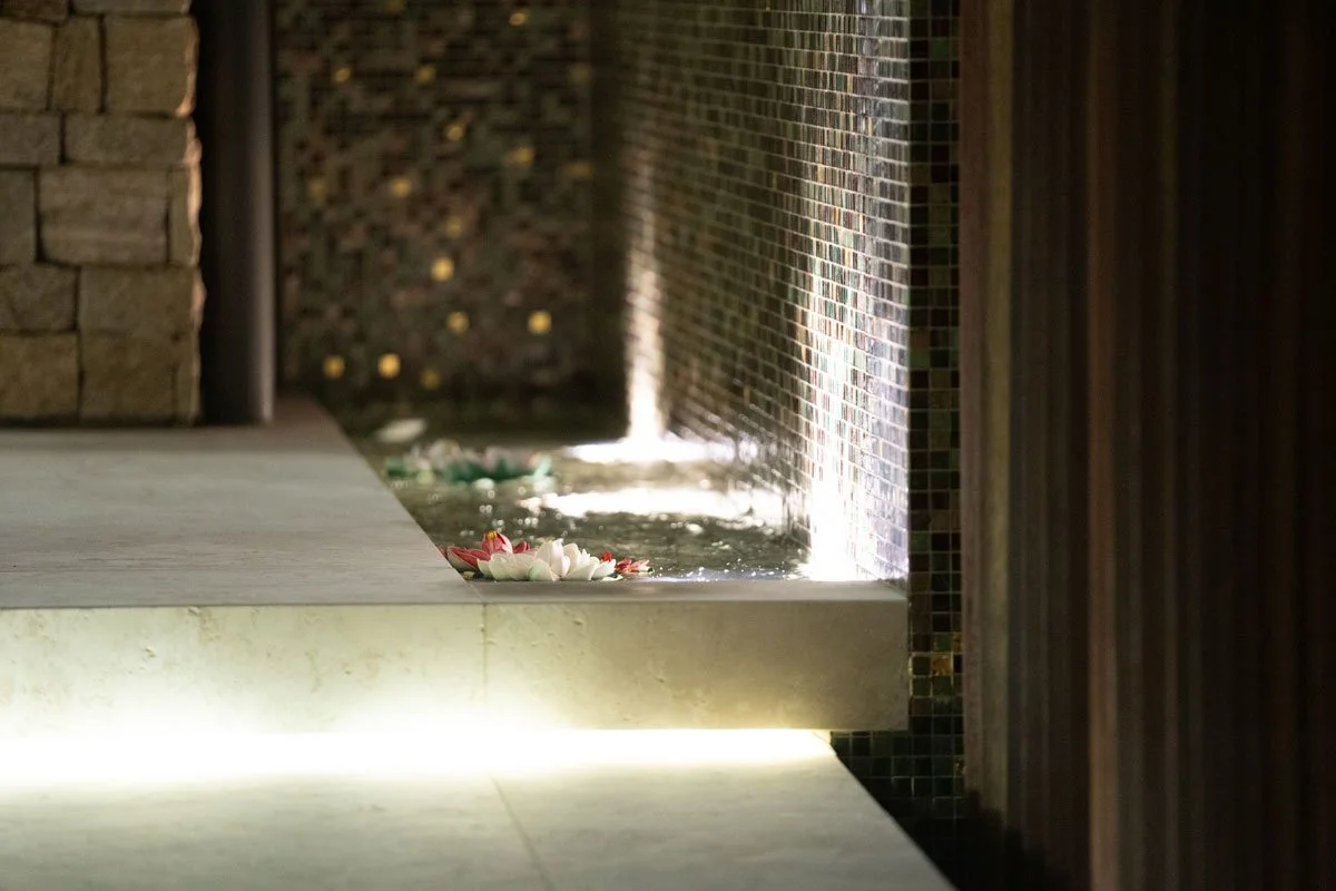 Indoor water feature with floating flowers, wooden and tiled walls, and soft lighting.