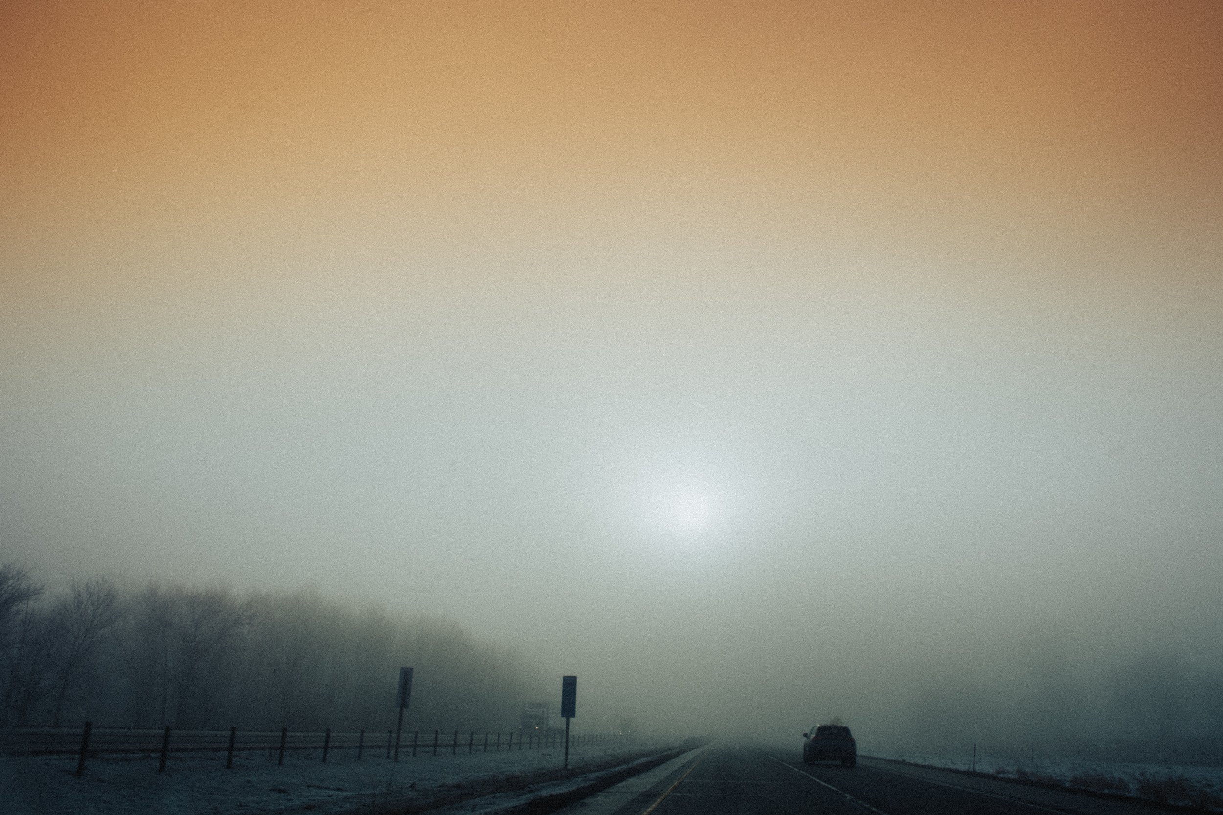 A car driving on a foggy highway with a blurred background of trees and a pale sky.