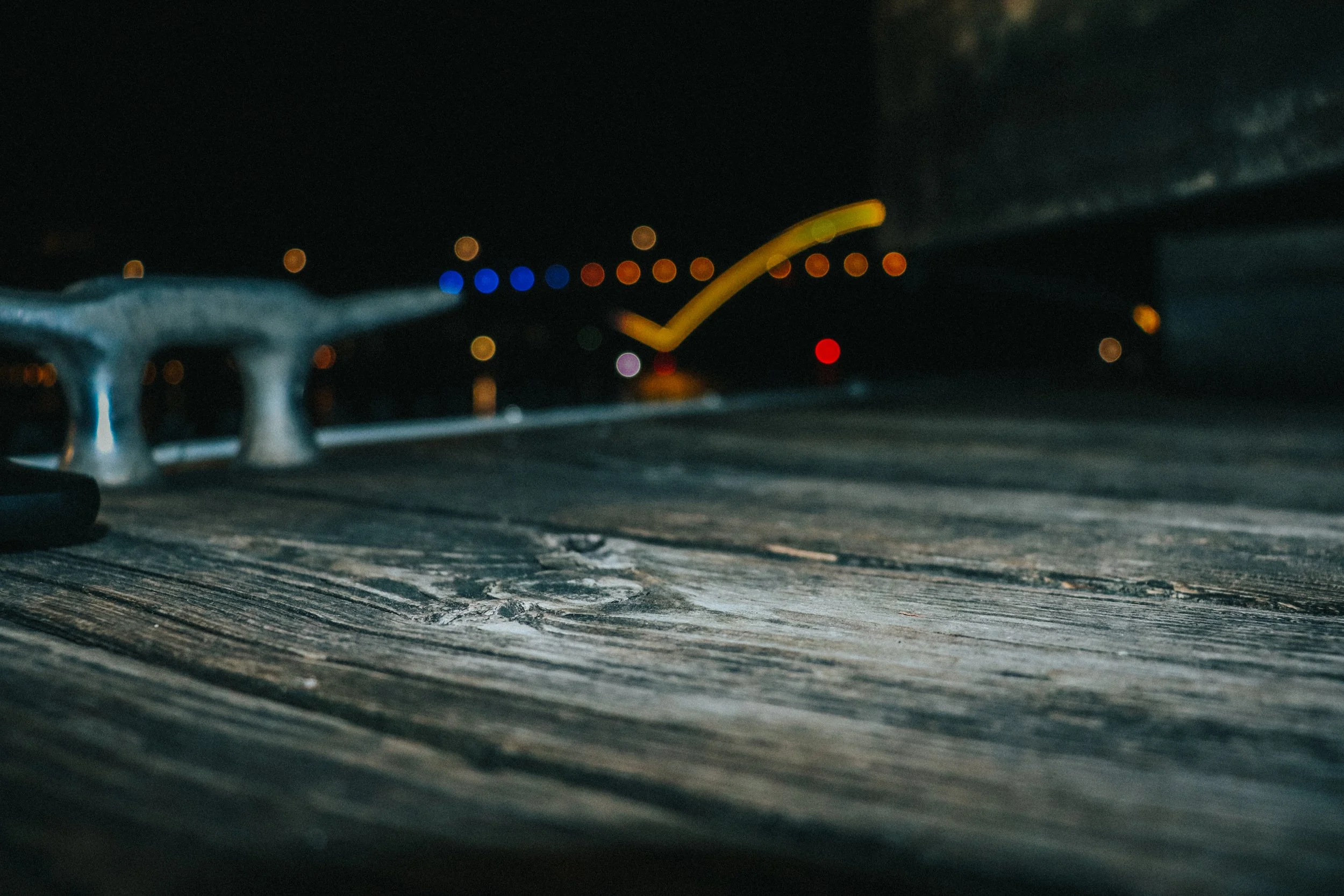 Close-up of a level on a carpenter's spirit level resting on a wooden surface at night, with blurred city lights in the background.