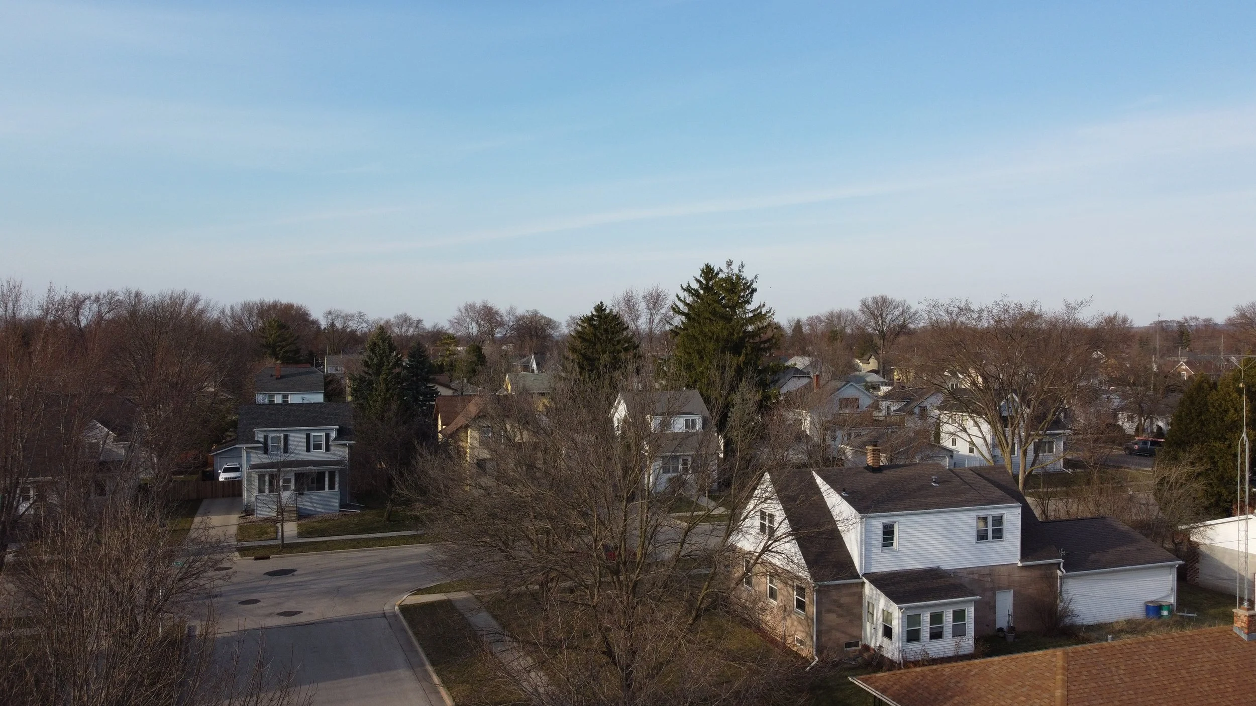 Aerial view of a suburban neighborhood with houses, leafless trees, and a clear sky.