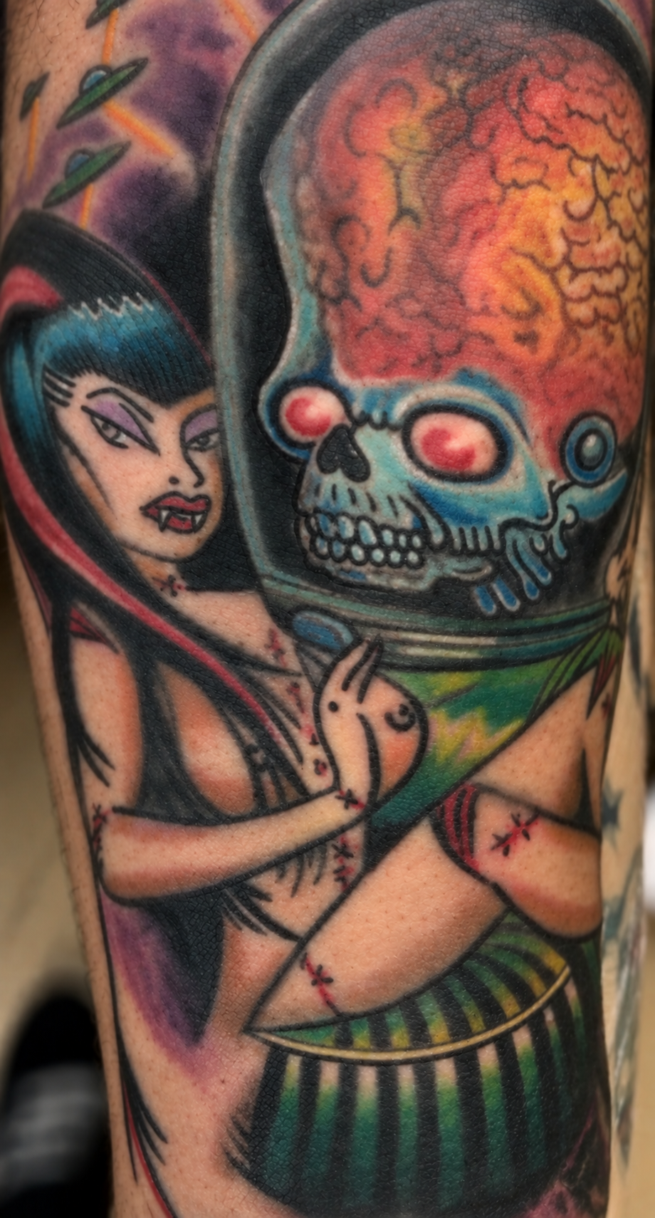 Tattoo of a woman with black hair and purple streaks, holding a crystal ball with a colorful brain inside, depicted as a skull, on her arm.